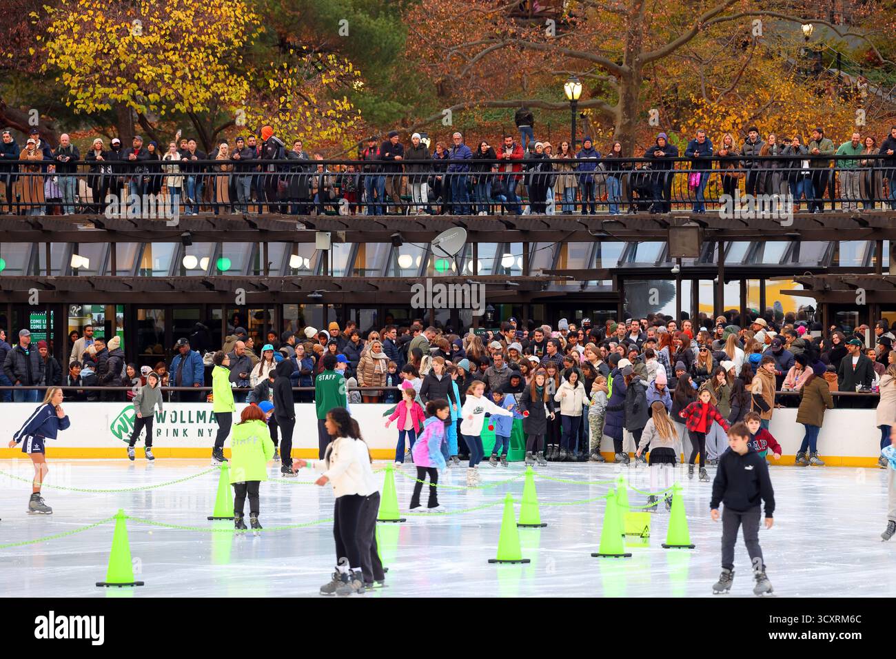Eisläufer betreten eine frisch aufgefrischte Eislaufbahn am Wollman Rink im Central Park in Manhattan, New York City, während die Zuschauer von oben beobachten. Stockfoto