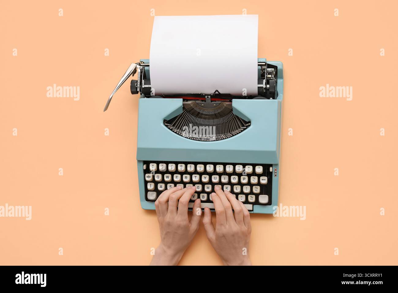 Frau tippt auf Schreibmaschine mit leerem Papierbogen auf beigem Hintergrund Stockfoto