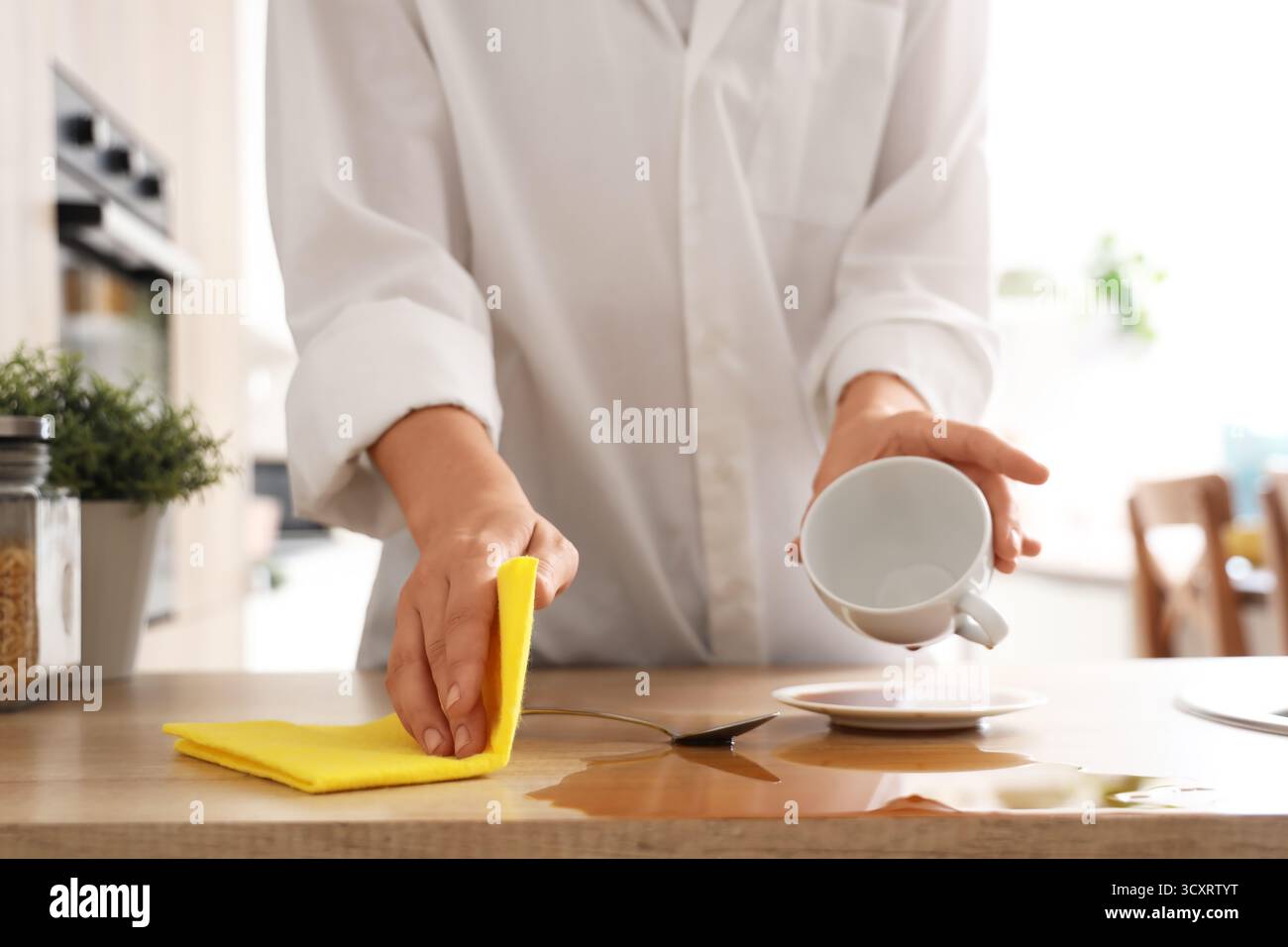 Frau, die mit einem Lappen verschütteten Kaffee auf dem Tisch in der Küche abwischt, Nahaufnahme Stockfoto