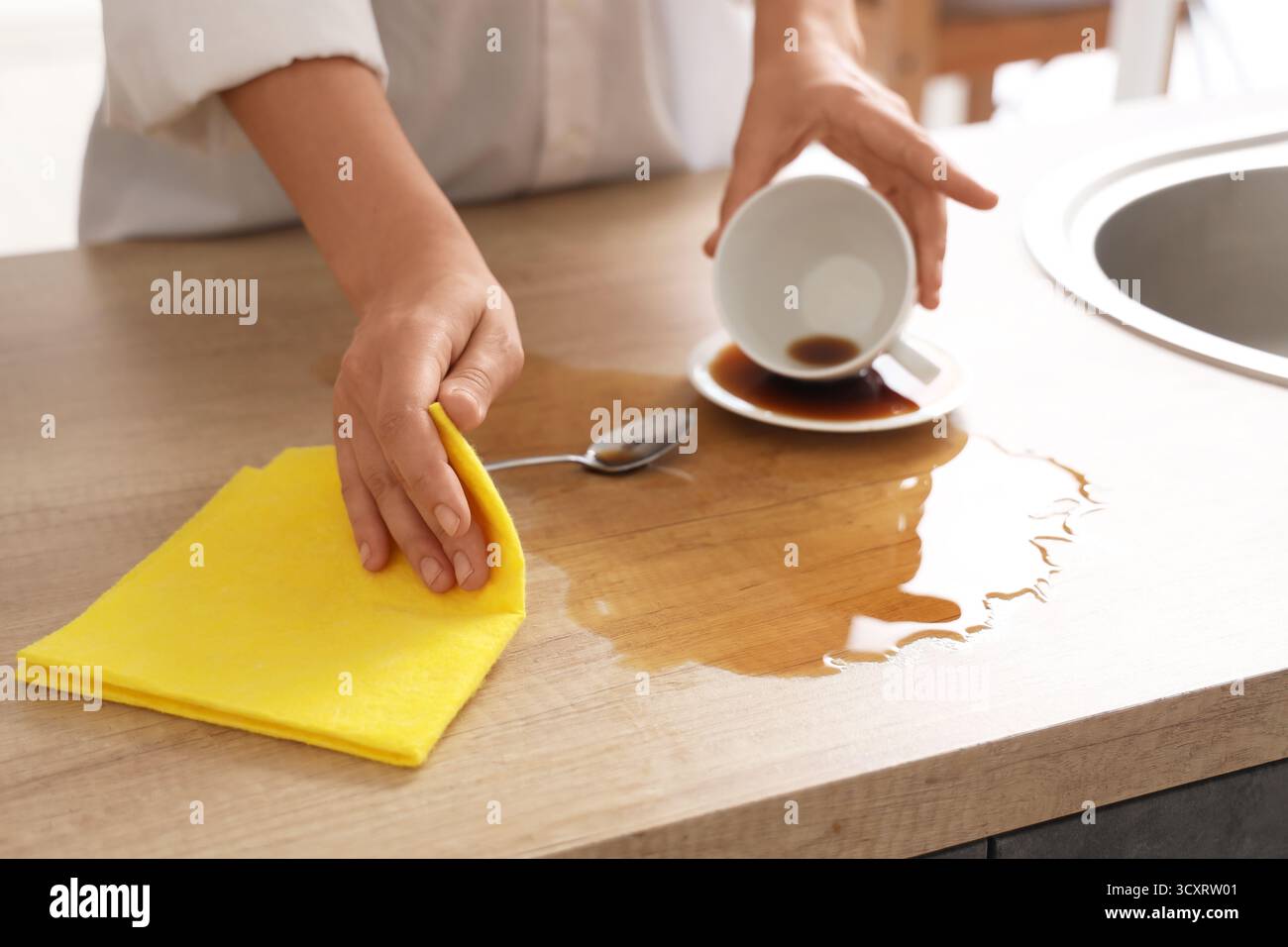 Frau, die mit einem Lappen verschütteten Kaffee auf dem Tisch in der Küche abwischt, Nahaufnahme Stockfoto