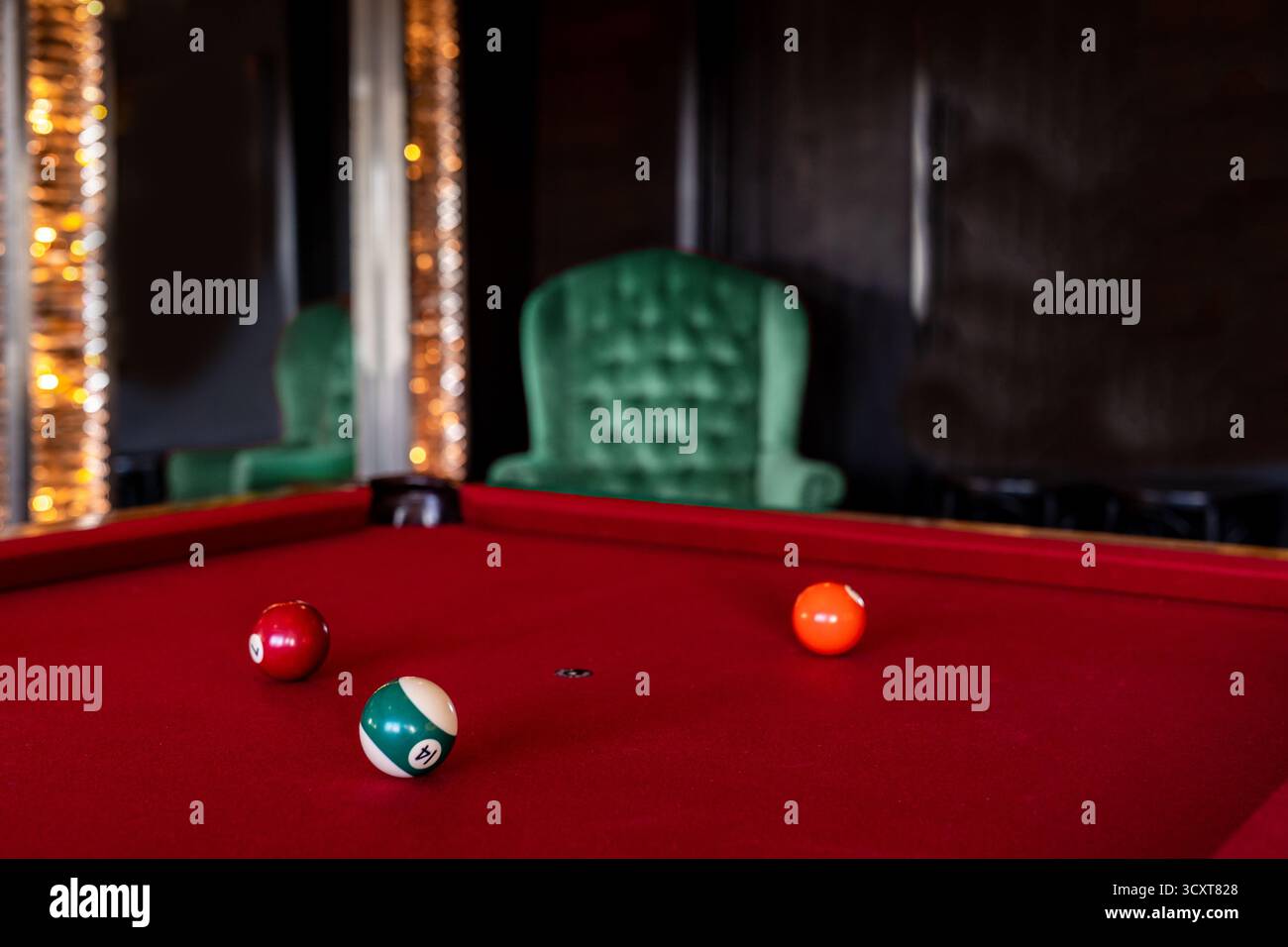 Roter Billardtisch mit Kugeln in einem luxuriösen Zimmer mit Samtstuhl und elegantem Spiegel Stockfoto