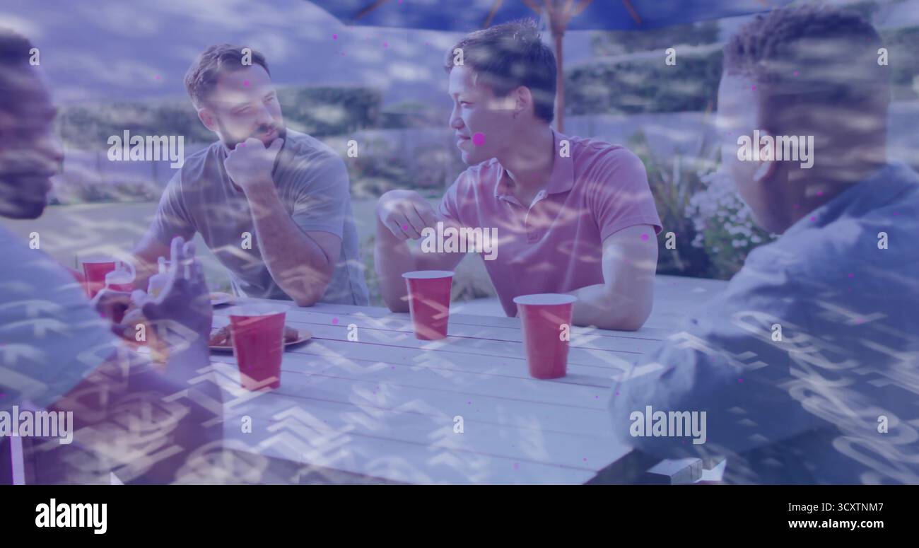 Lachende vier Freunde, die an einem Picknicktisch auf der Terrasse im Hinterhof unter einem Sonnenschirm sitzen, mit roten Tassen Stockfoto
