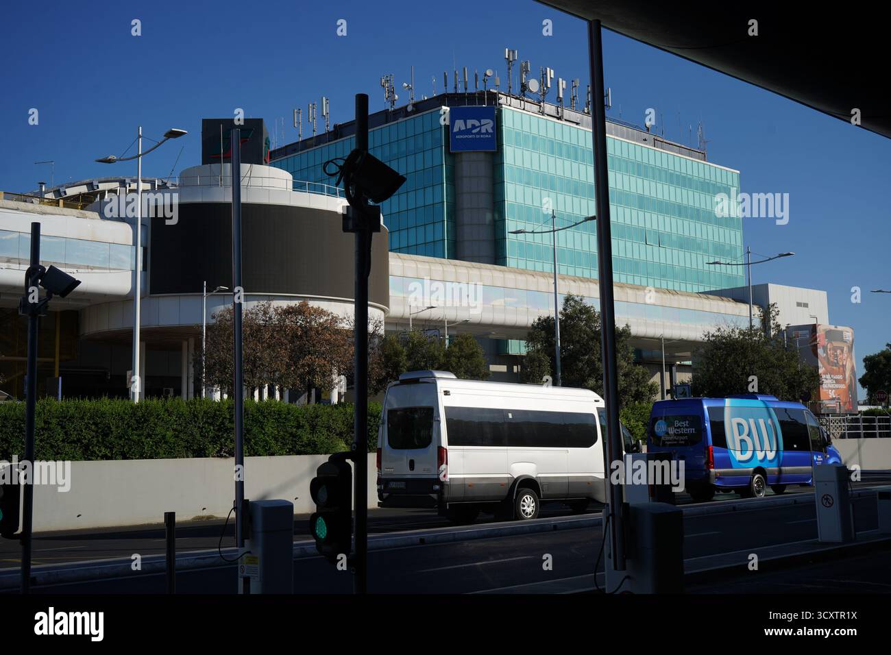 Das blaue ADR-Gebäude am Flughafen Fiumicino in Rom, Italien, ragt über Shuttle-Vans und symbolisiert internationale Reisen und moderne Infrastruktur. Stockfoto