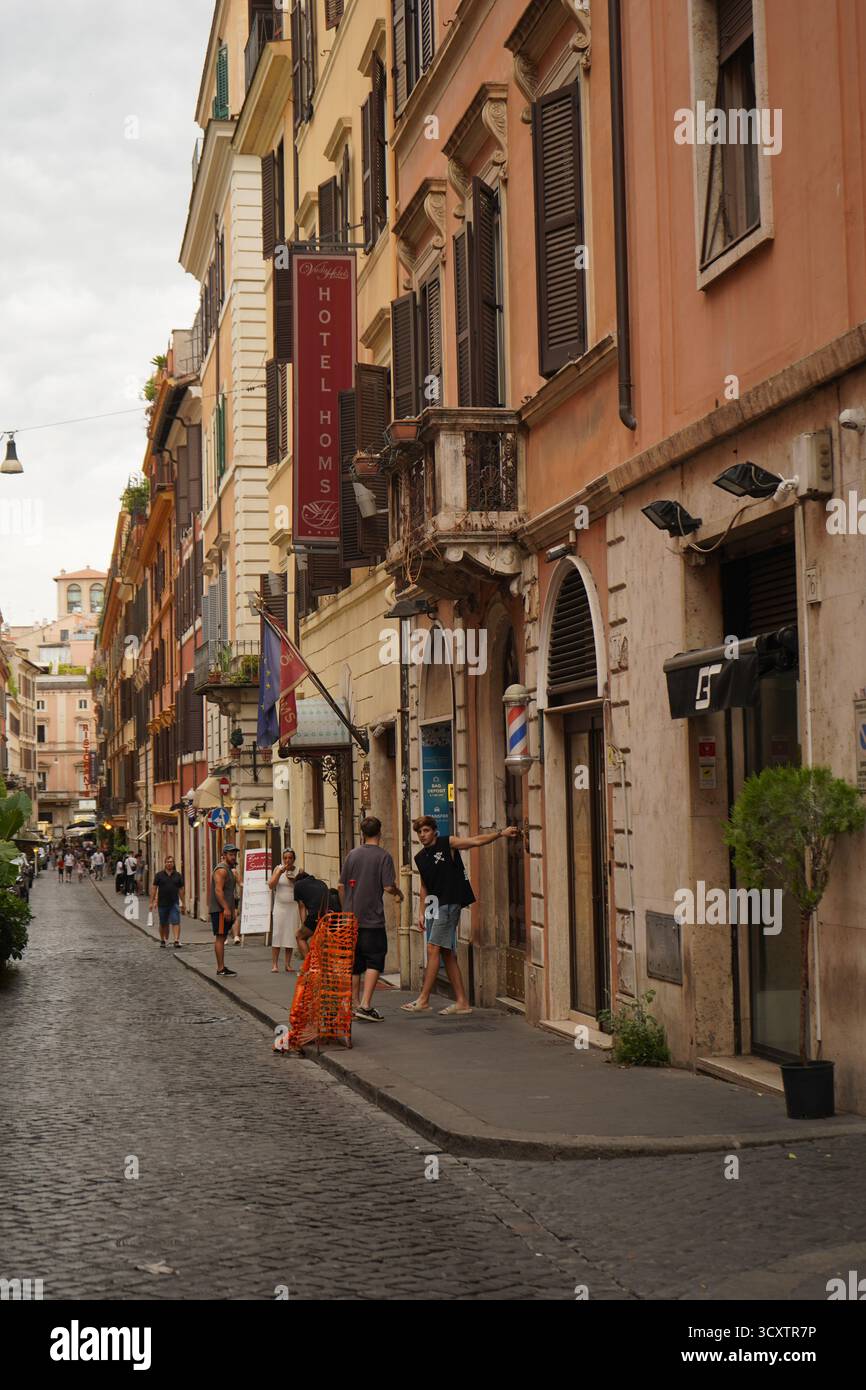 Straßenszene aus Kopfsteinpflaster in Rom mit dem Hotel Homs an der Via della Vite, das charakteristische Pastellgebäude und Spaziergänge zeigt. Stockfoto