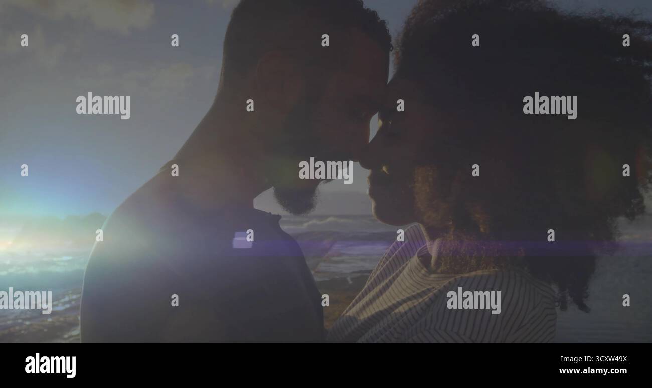 Romantisches Paar, das bei Sonnenuntergang am Sandstrand die Stirn berührt, mit sanften Wellen und Linsenflecken Stockfoto