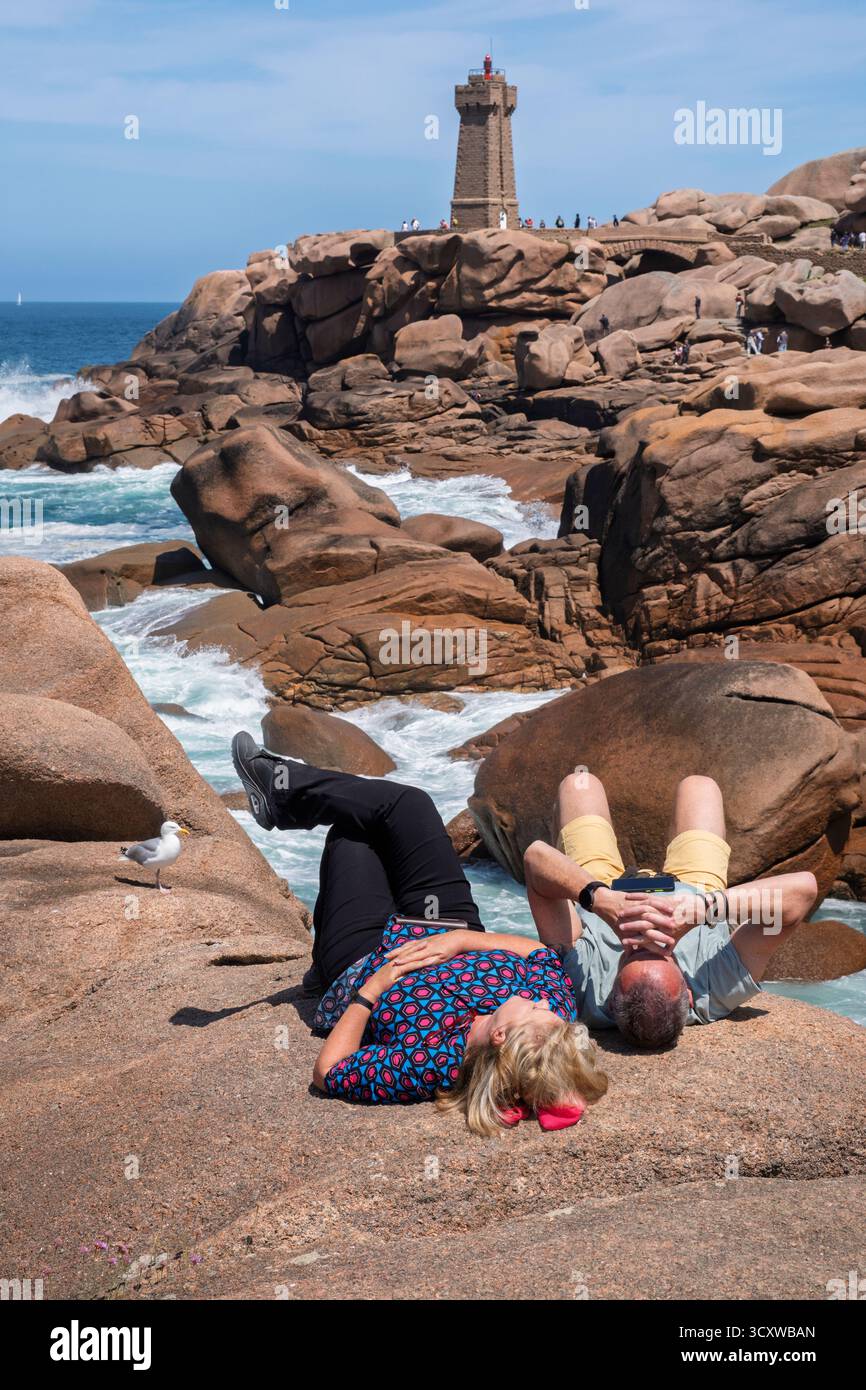 Touristen liegen auf den Felsen an der Côte de Granit Rose in der Nähe des Leuchtturms 'Phare de Men Ruz', Ploumanac'h, Côtes-d'Armor, Bretagne Stockfoto