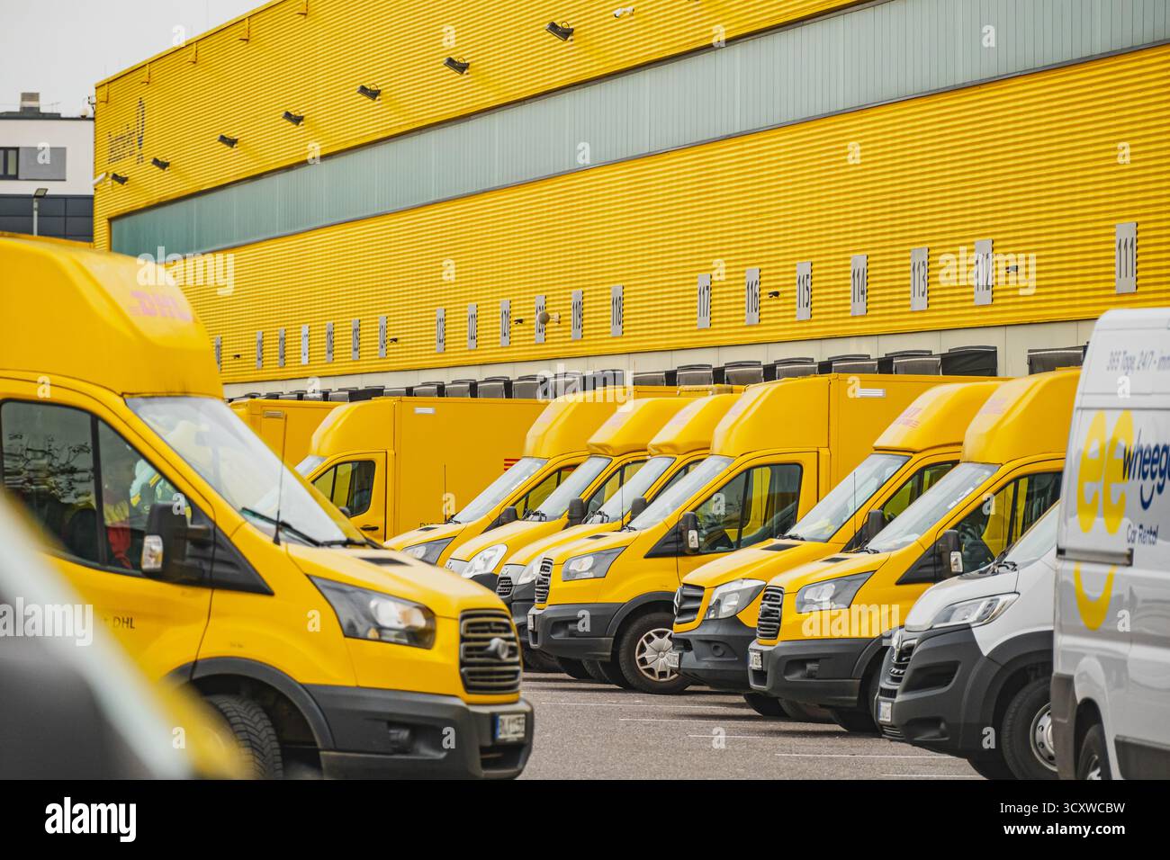 Reihen geparkter gelber Lieferwagen vor dem DHL Logistiklager Stockfoto