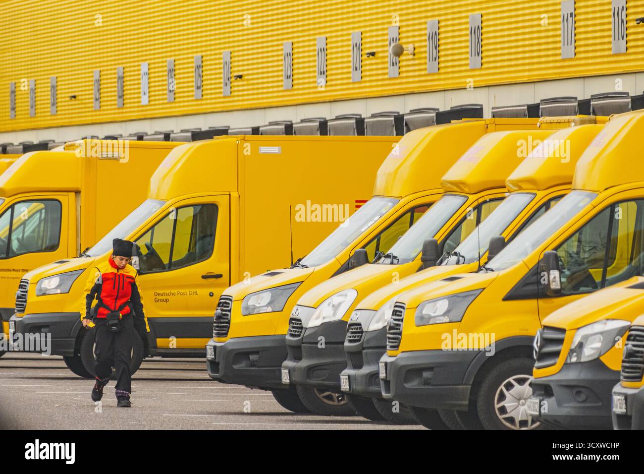 Reihen geparkte gelbe Lieferwagen vor dem DHL Logistiklager, an denen ein Mitarbeiter vorbeifährt Stockfoto