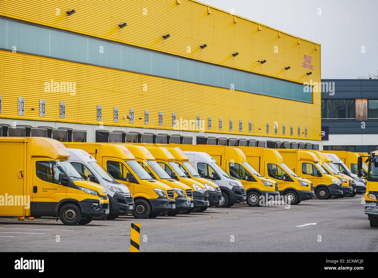 Reihen geparkter gelber Lieferwagen vor dem DHL Logistiklager Stockfoto