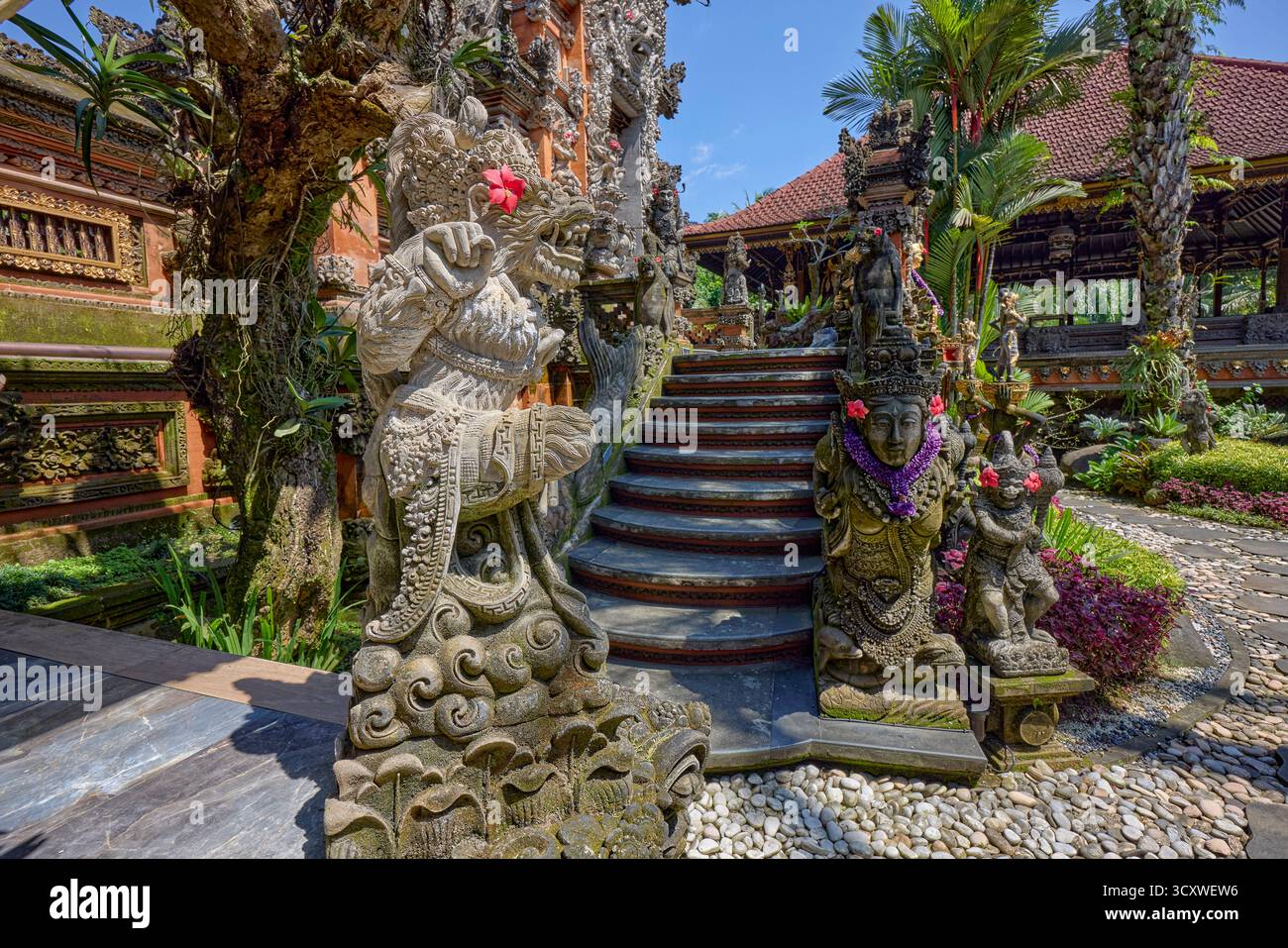 Aufwändig geschnitzte Steinstatuen, die mit Blumen verziert sind, am Puri Langon Tempel in Ubud, Gianyar, Bali, Indonesien. Stockfoto