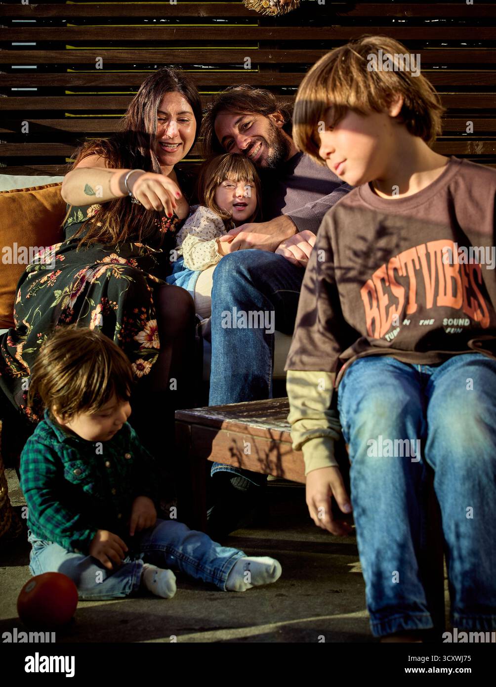 Eine Familie mit 5 Personen sitzt im Herbst im Freien unter warmem Sonnenlicht und teilt einen ruhigen Moment. Schatten und Licht sorgen für Gruppenharmonie Stockfoto