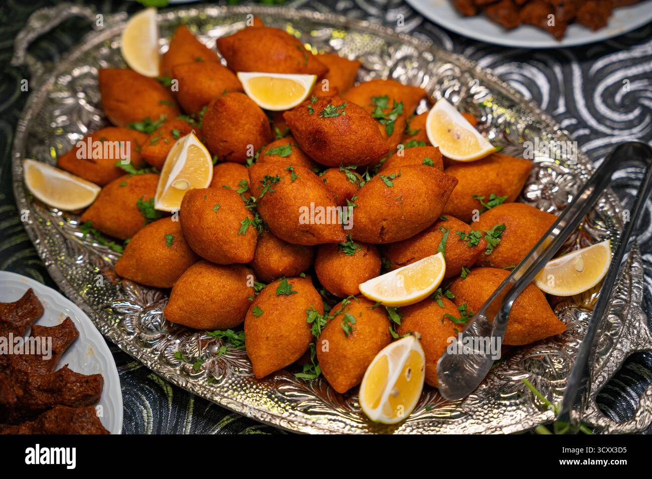 Traditionelle türkische und Arap Icli Kofte serviert mit Zitronenscheiben auf Silbertablett. Goldene gebratene Bulgur-Fleischbällchen Kibbeh. Beliebtes Gericht Stockfoto