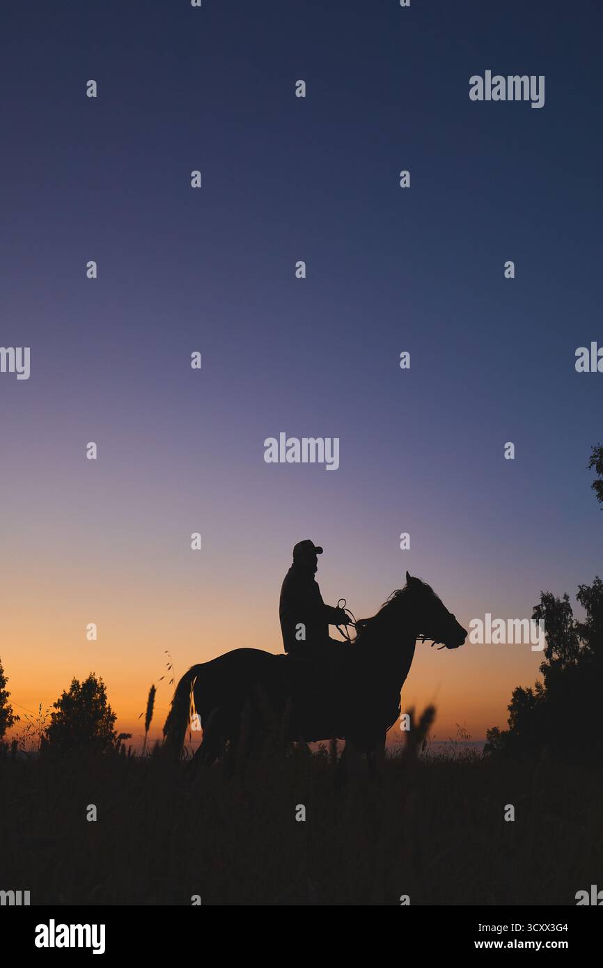 Silhouette eines Mannes, der bei Sonnenuntergang auf einem Pferd reitet Stockfoto