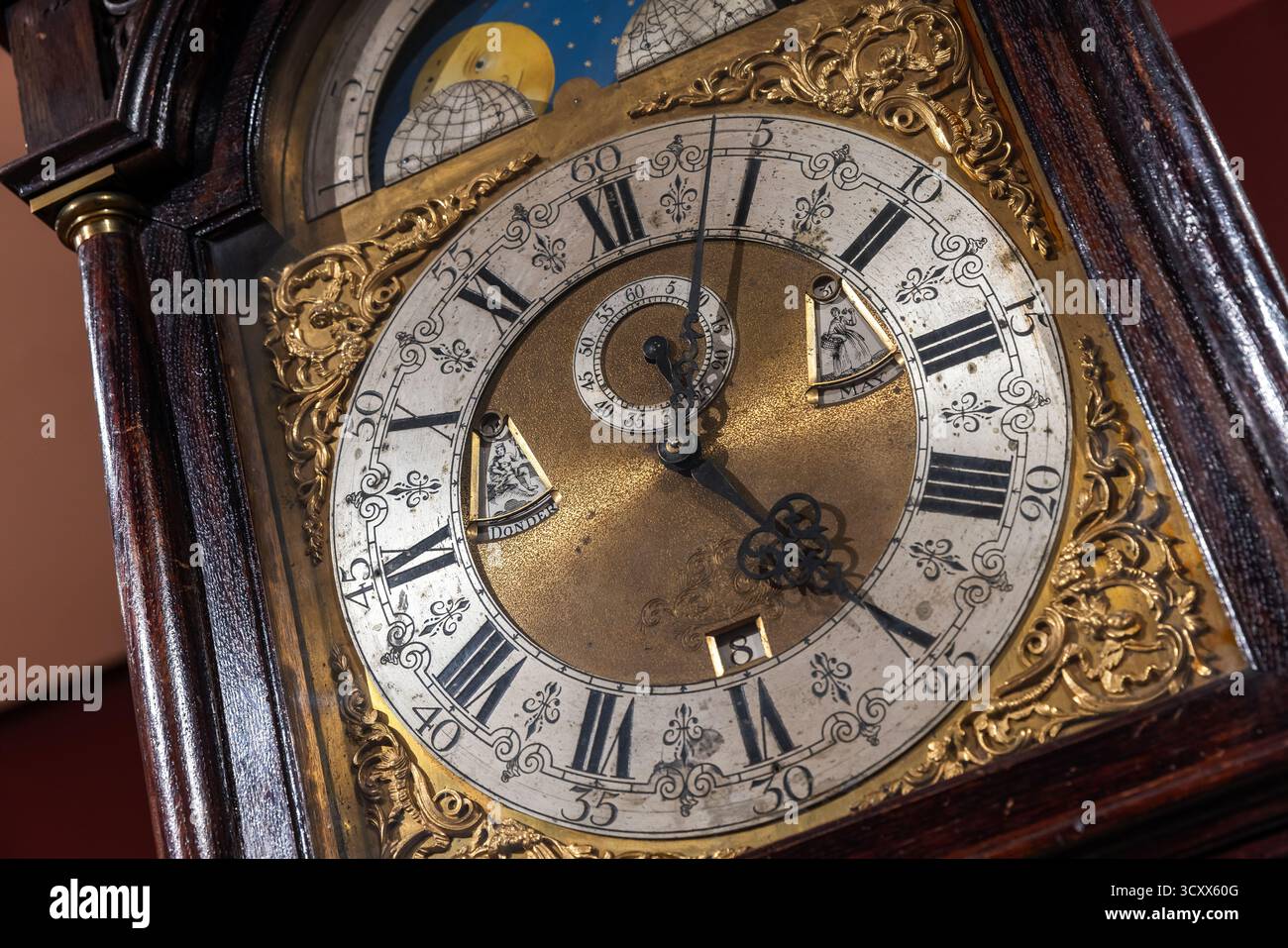 Eine detailgetreue Aufnahme einer Vintage-Großvateruhr mit Messingmitte, filigranem Gold und einem römischen Zifferblatt. Reichhaltiges Holzkoffer und Mondschein Stockfoto