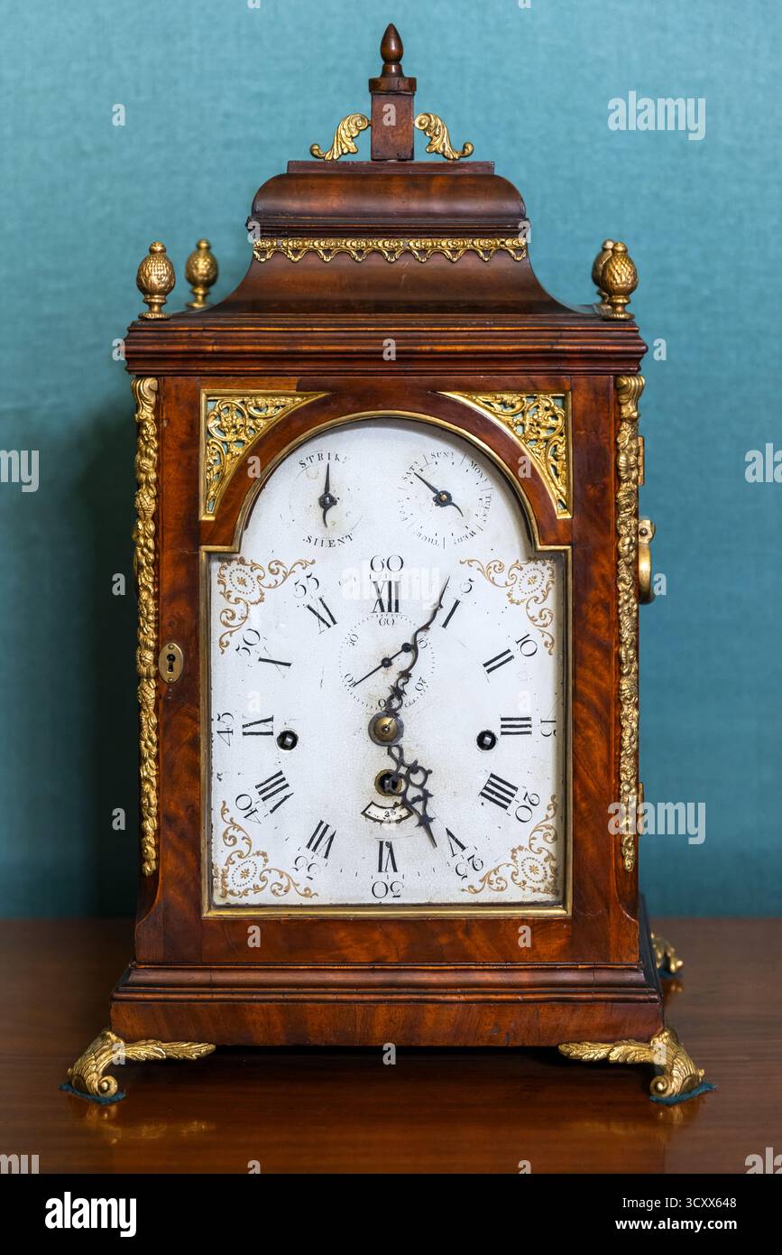 Eine reich geschnitzte antike hölzerne Uhr verfügt über vergoldete Akzente und verzierte Messingdetails. Diese Vintage-Uhr strahlt Eleganz, historischen Charme und aus Stockfoto