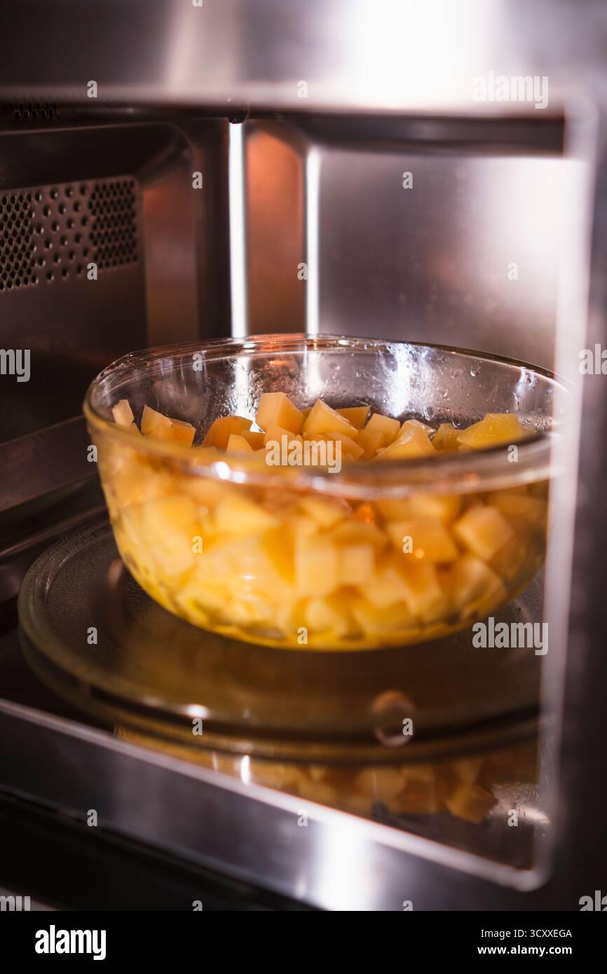 Stellen Sie eine Schüssel mit rohen geschälten Kartoffeln in die Mikrowelle. Zuhause kochen. Frisches hausgemachtes Essen. Stockfoto