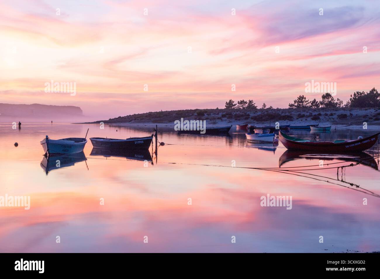 Kleine Fischerboote schwimmen ruhig auf reflektierendem Wasser unter einem lebhaften Sonnenuntergang Stockfoto