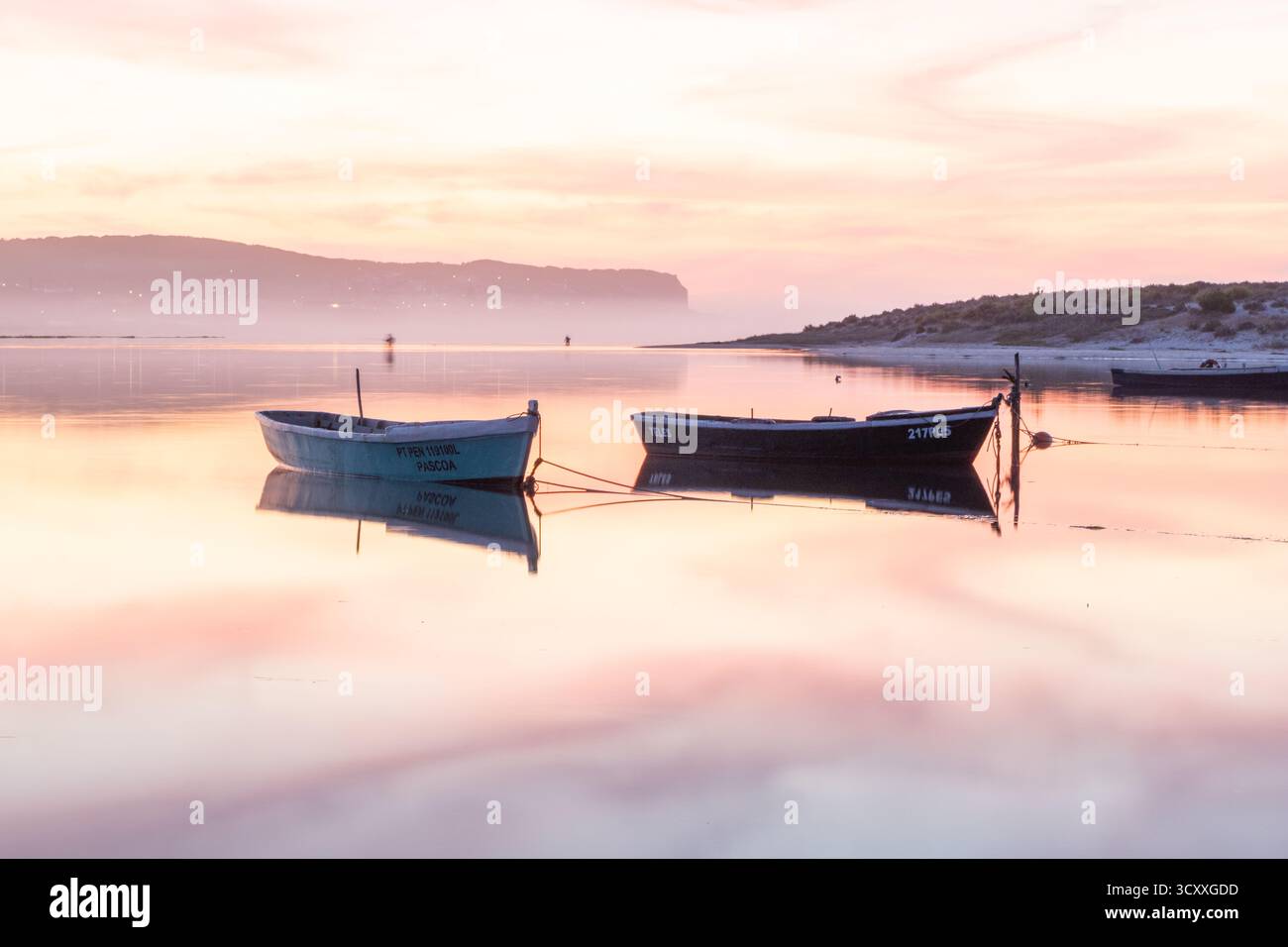 Kleine Fischerboote, die auf stillem Wasser schweben und einen farbenfrohen Sonnenuntergangshimmel reflektieren Stockfoto