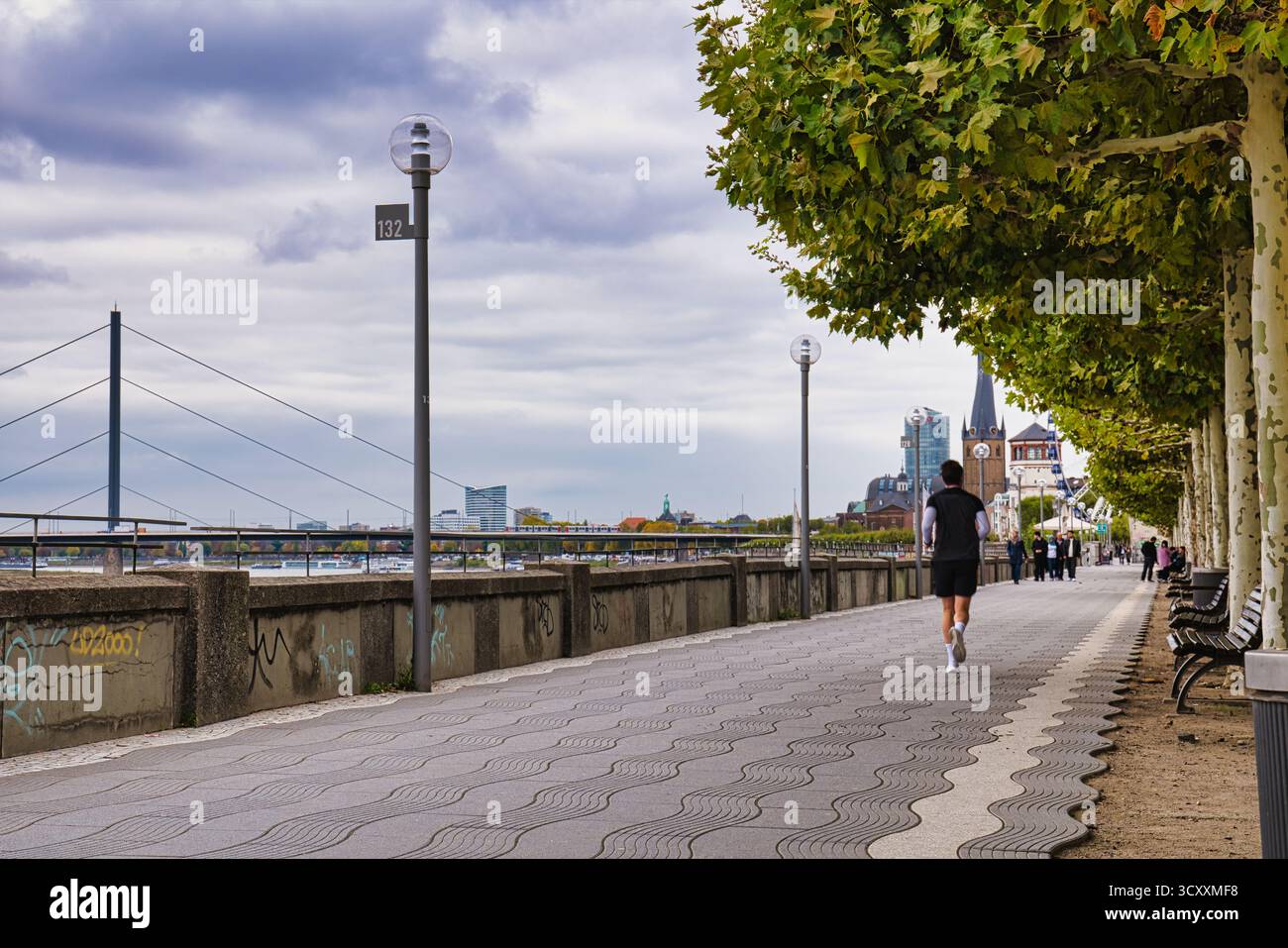 Joggen auf der von Bäumen gesäumten Rheinpromenade mit historischem Uhrenturm und City Skyline im Herbst Düsseldorf Deutschland Stockfoto