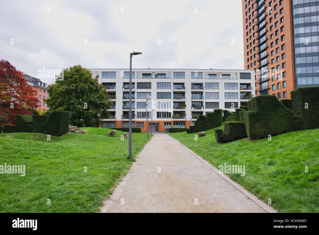 Ruhiger Pfad führt durch den üppigen Green Park mit kunstvollen Hecken und modernen Wohngebäuden unter dem bewölkten Herbsthimmel Stockfoto