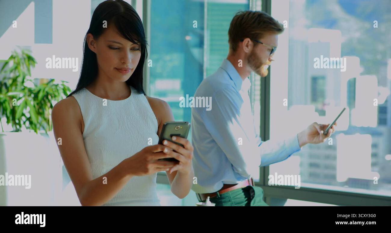 Stehende Ureinwohner-Frau und weißer Mann, die Smartphones im Büro benutzen, mit Pflanzen, Wandskizzen Stockfoto