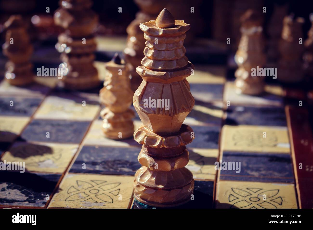 Eine wunderschöne handgefertigte hölzerne Schachspielkönigin, die auf einem karierten Brett im warmen Sonnenlicht steht, strategisches Spielkonzept, intellektuelle Herausforderung, nah Stockfoto