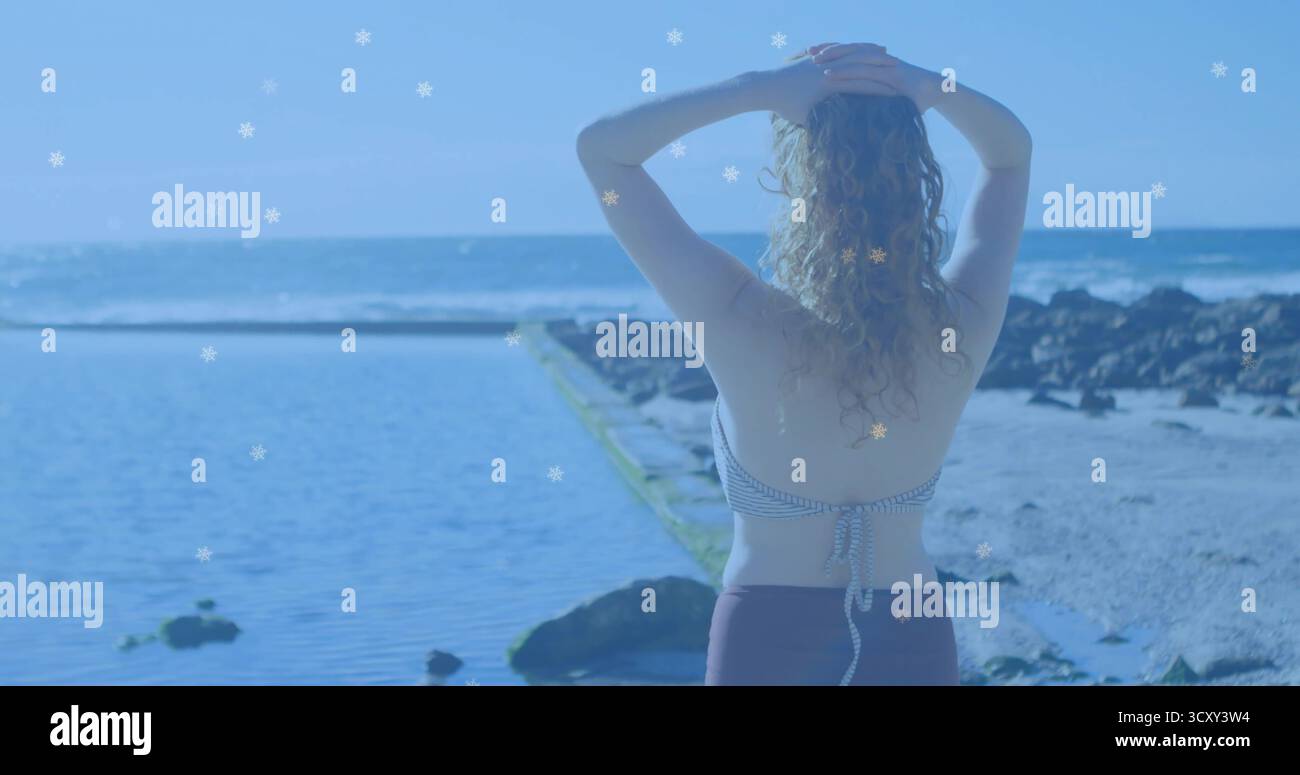 Stehende Frau in gestreiftem Badeanzug, die in Richtung Horizont blickt, auf den Gezeitenpool mit vulkanischen Felsen Stockfoto