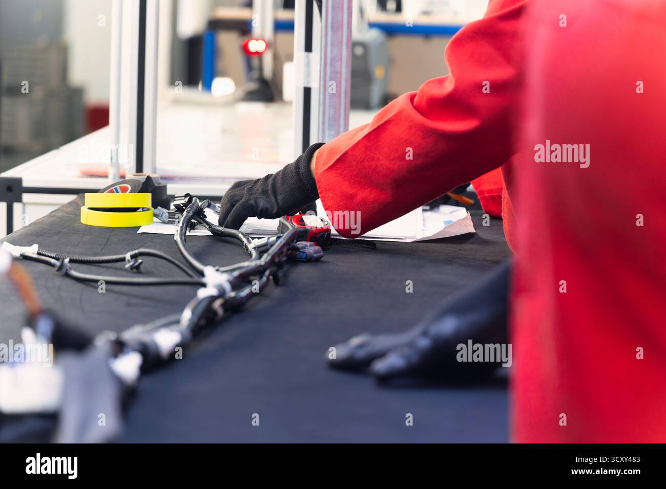 afroamerikanischer Arbeiter in einer Elektrofabrik für Kabelbäume in der Automobilfabrik, der die Verkabelung und die Steckverbinder auf einer Vorlagenplatte erledigt Stockfoto