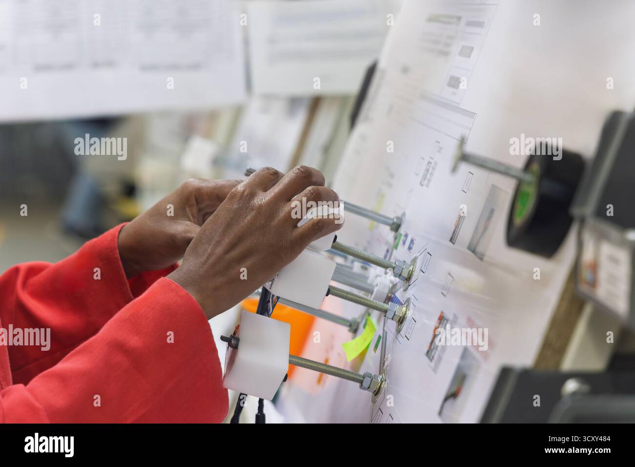 afroamerikanischer Arbeiter in einer Elektrofabrik für Kabelbäume in der Automobilfabrik, der die Verkabelung und die Steckverbinder auf einer Vorlagenplatte erledigt Stockfoto
