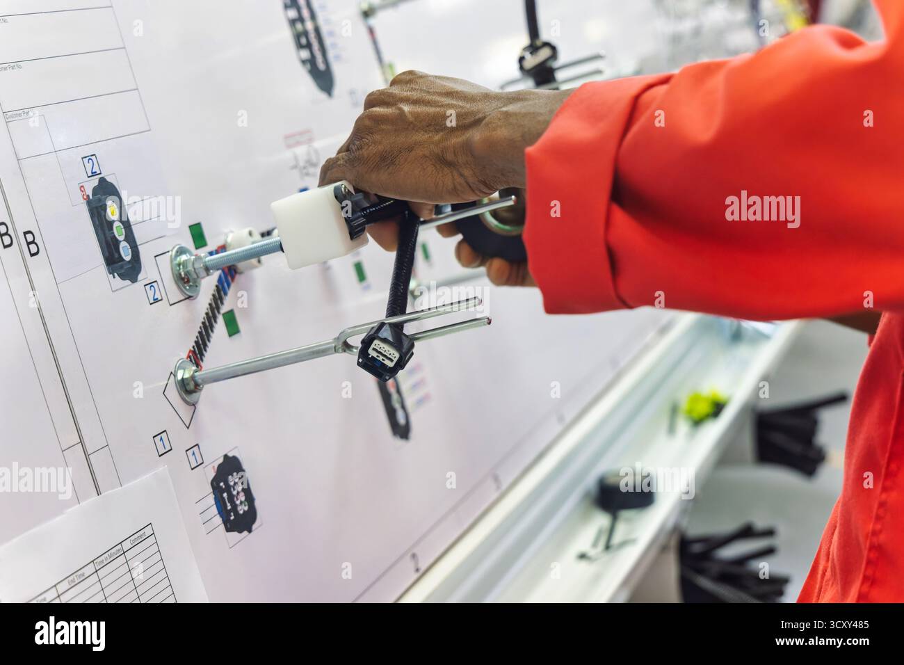 afroamerikanischer Arbeiter in einer Elektrofabrik für Kabelbäume in der Automobilfabrik, der die Verkabelung und die Steckverbinder auf einer Vorlagenplatte erledigt Stockfoto