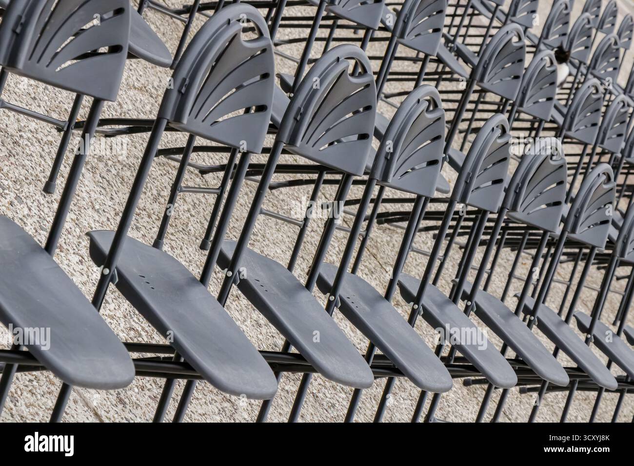 Perspektivische Ansicht mehrerer Reihen identischer schwarzer Stühle, die auf einer strukturierten Steinoberfläche angeordnet sind. Die Komposition betont Rhythmus, Geometrie und Org Stockfoto