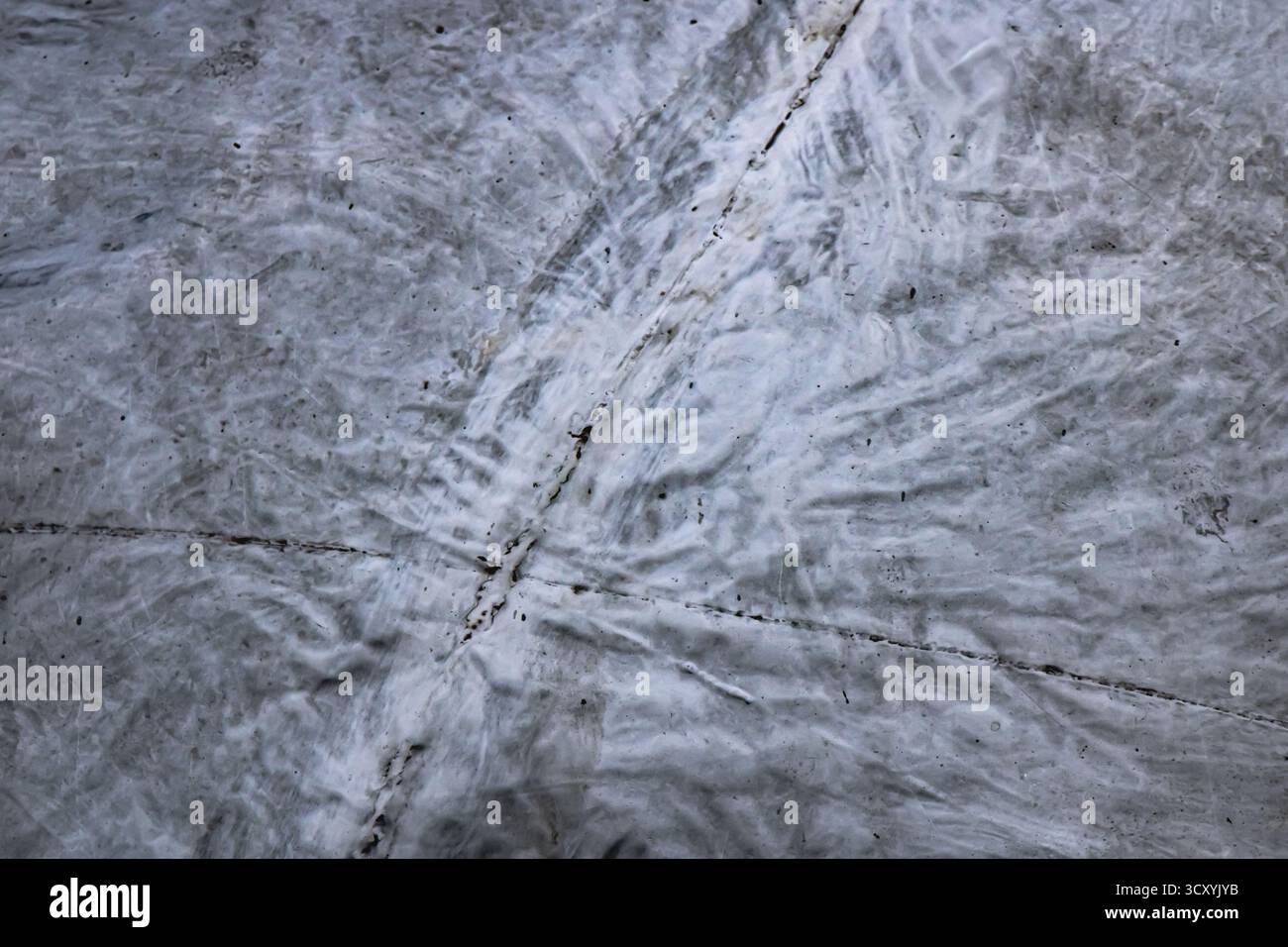 Detaillierte Nahaufnahme einer grauen Betonoberfläche mit sich schneidenden Rissen, subtilen Mustern und Oberflächenverschleiß bei Tageslicht – das raue urbane t einfangen Stockfoto