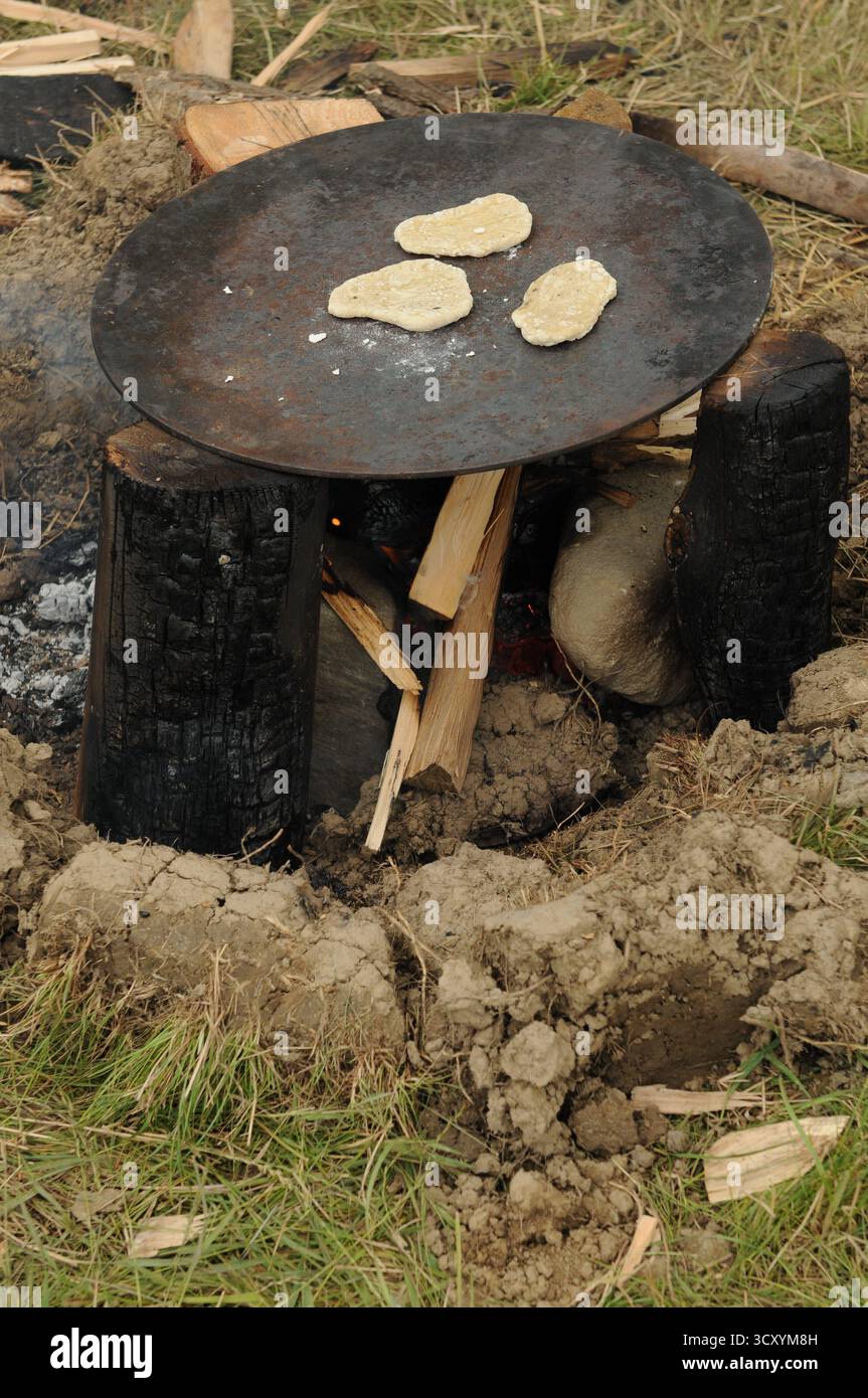 Fladenbrote, die auf einer eisernen Platte über einem offenen Feuer während einer frühmittelalterlichen Kochdemonstration in Trzcinica, Subkarpaten, Polen, backen. Stockfoto