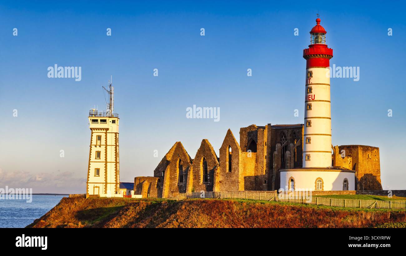 Der hohe Leuchtturm Phare de Saint-Mathieu steht neben den Überresten einer alten Steinabtei. Die untergehende Sonne wirft warmes Licht und hebt die Küste hervor Stockfoto