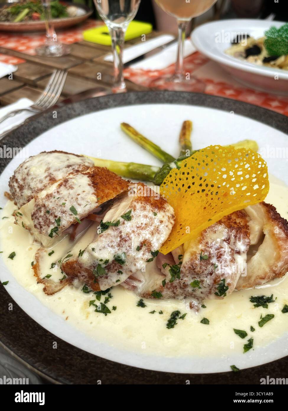 Gourmet-Gericht mit gegrilltem Huhn mit cremiger Sauce, Spargel und dekorativen Elementen auf einem eleganten Esstisch Stockfoto