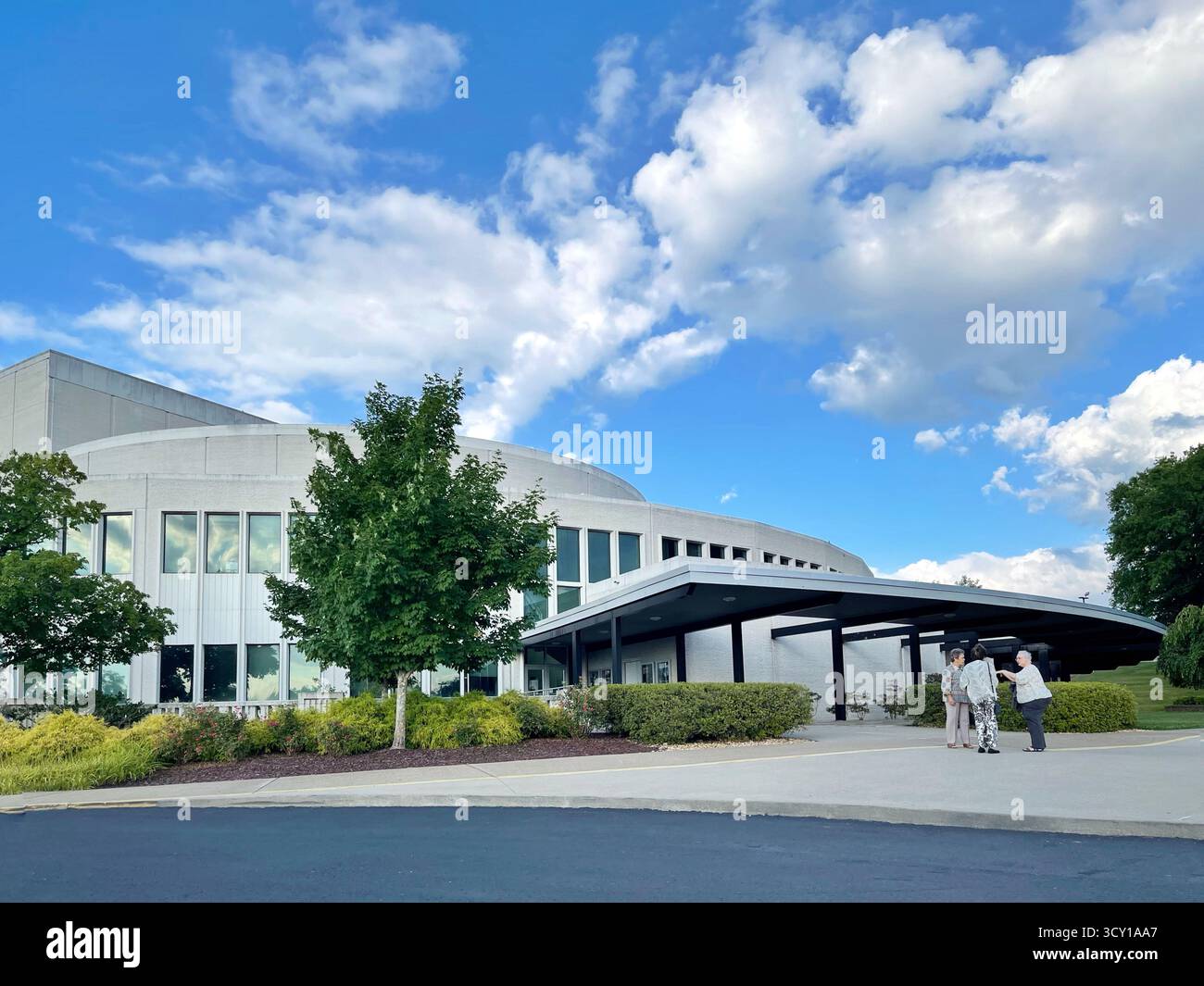 WVU Creative Arts Center – modernes öffentliches Gebäude mit geschwungener Fassade unter einem leuchtend blauen Himmel und verstreuten Wolken, vor denen sich Menschen versammeln. Stockfoto