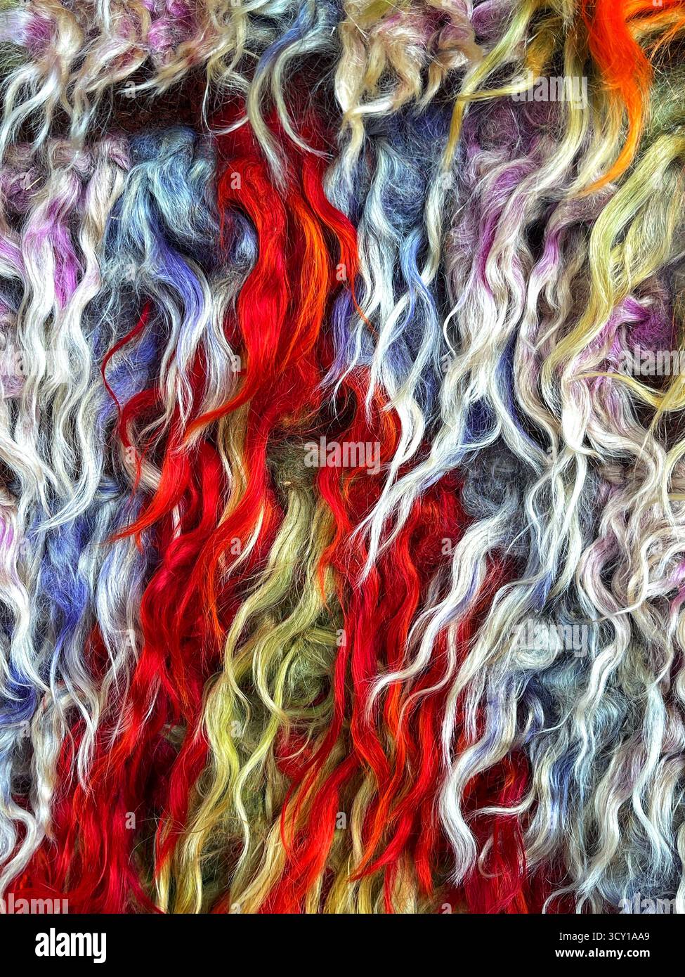 Lebendige Nahaufnahme aus mehrfarbigen Wollfasern mit lockiger Textur, die in einem dynamischen Muster angeordnet ist und für einen satten visuellen Effekt sorgt - Smartphone-aufgenommenes Stockfoto