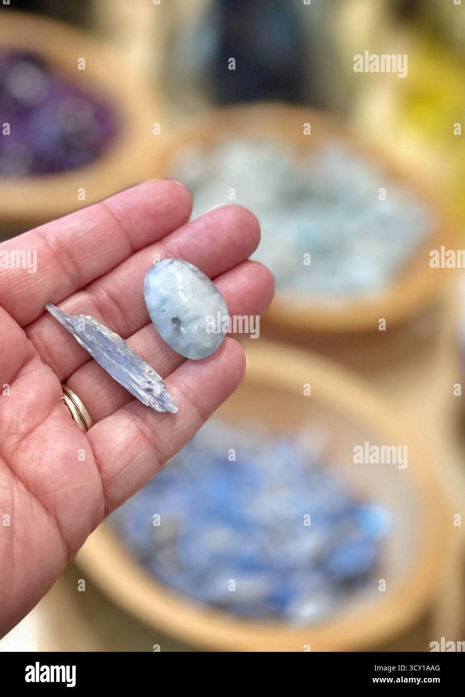 Nahaufnahme einer Hand mit zwei polierten blauen Kristallen mit verschwommenen Edelsteinen im Hintergrund auf einem Markt oder einer Ladenanzeige Stockfoto