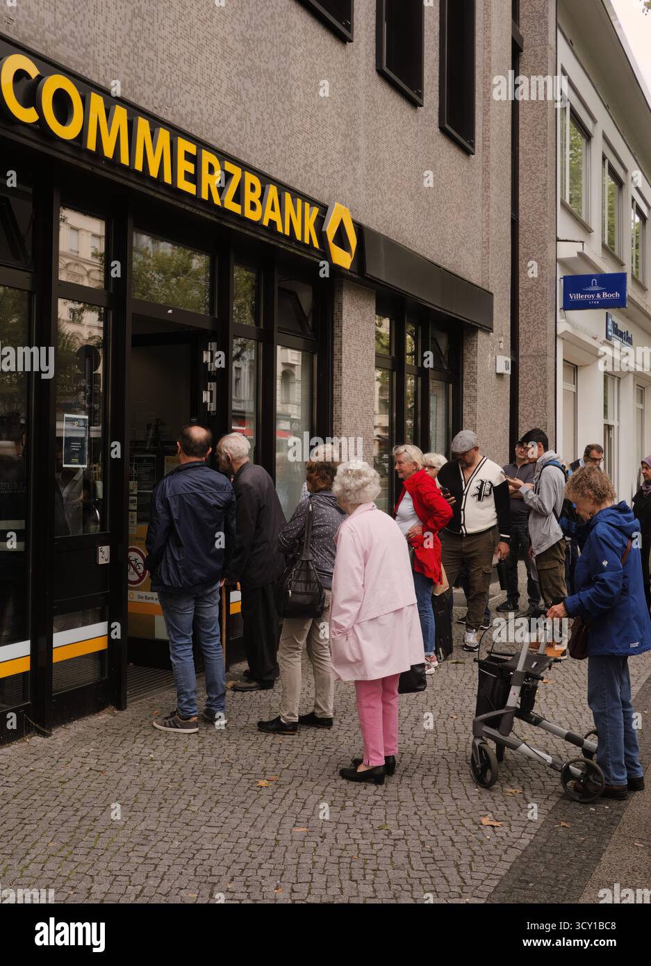 Schlange von verschiedenen Leuten vor einer deutschen Commerzbank. Bewölkt und realistisch. Deutet auf das tägliche Leben und die wirtschaftliche Interaktion hin. Stockfoto