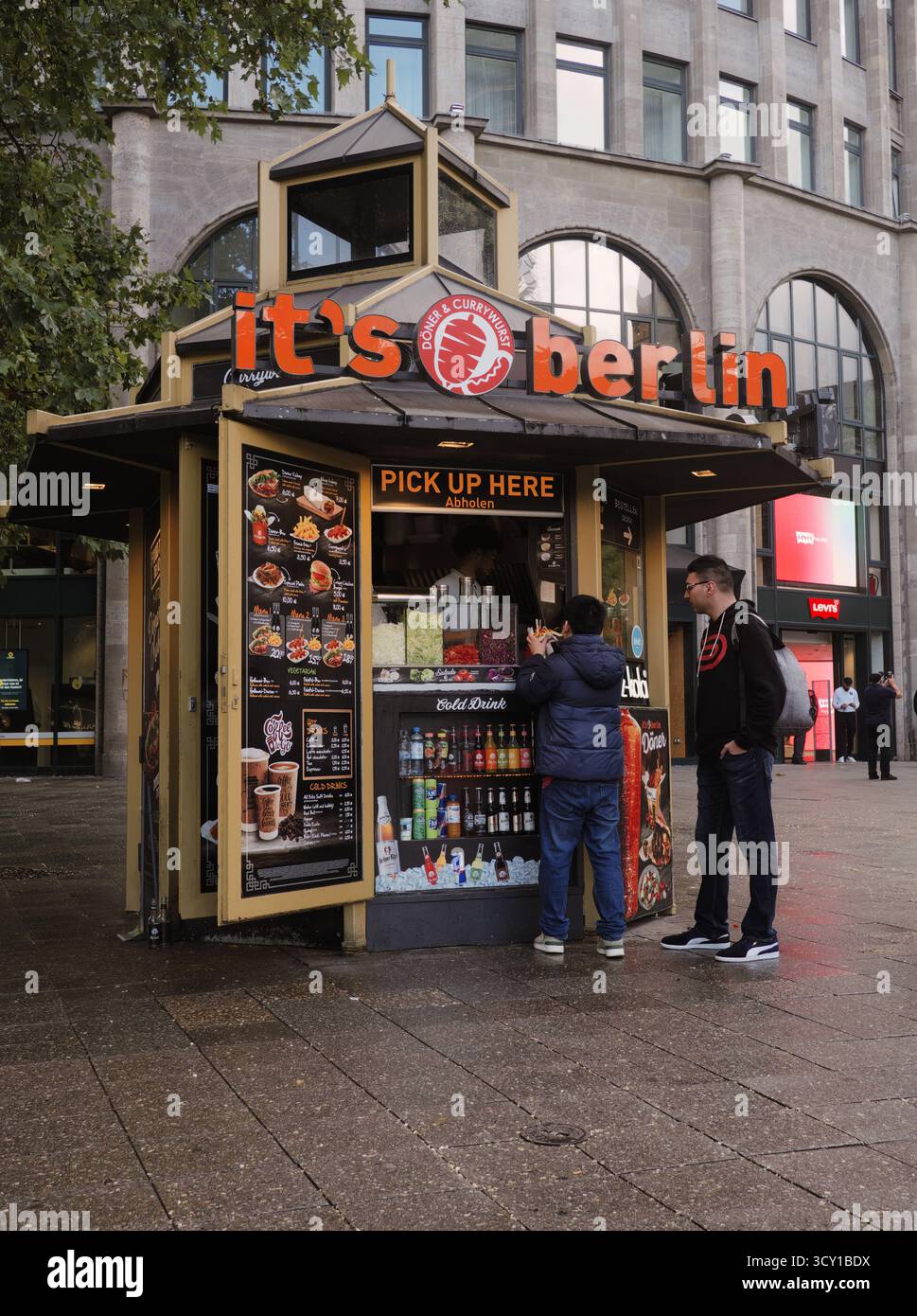 Currywurst und Döner: Berühmter Berliner Street Food Kiosk in der Abenddämmerung. Regnerische, reflektierende, authentische urbane Tonalität und Stimmung. Stockfoto