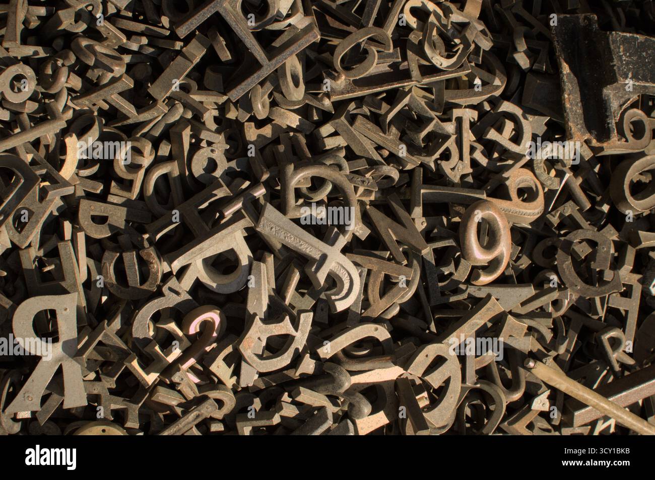 Ein chaotischer Haufen alter, rostiger Metallschriftformen. Dunkle, industrielle Tonalität ruft eine Stimmung von Geschichte, Komplexität und vergessenem Handwerk hervor. Stockfoto