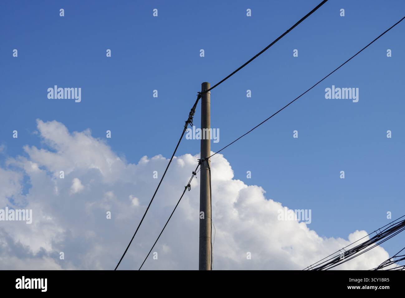 Ein Versorgungsmast mit Stromleitungen gegen einen blauen Himmel und Wolken Stockfoto