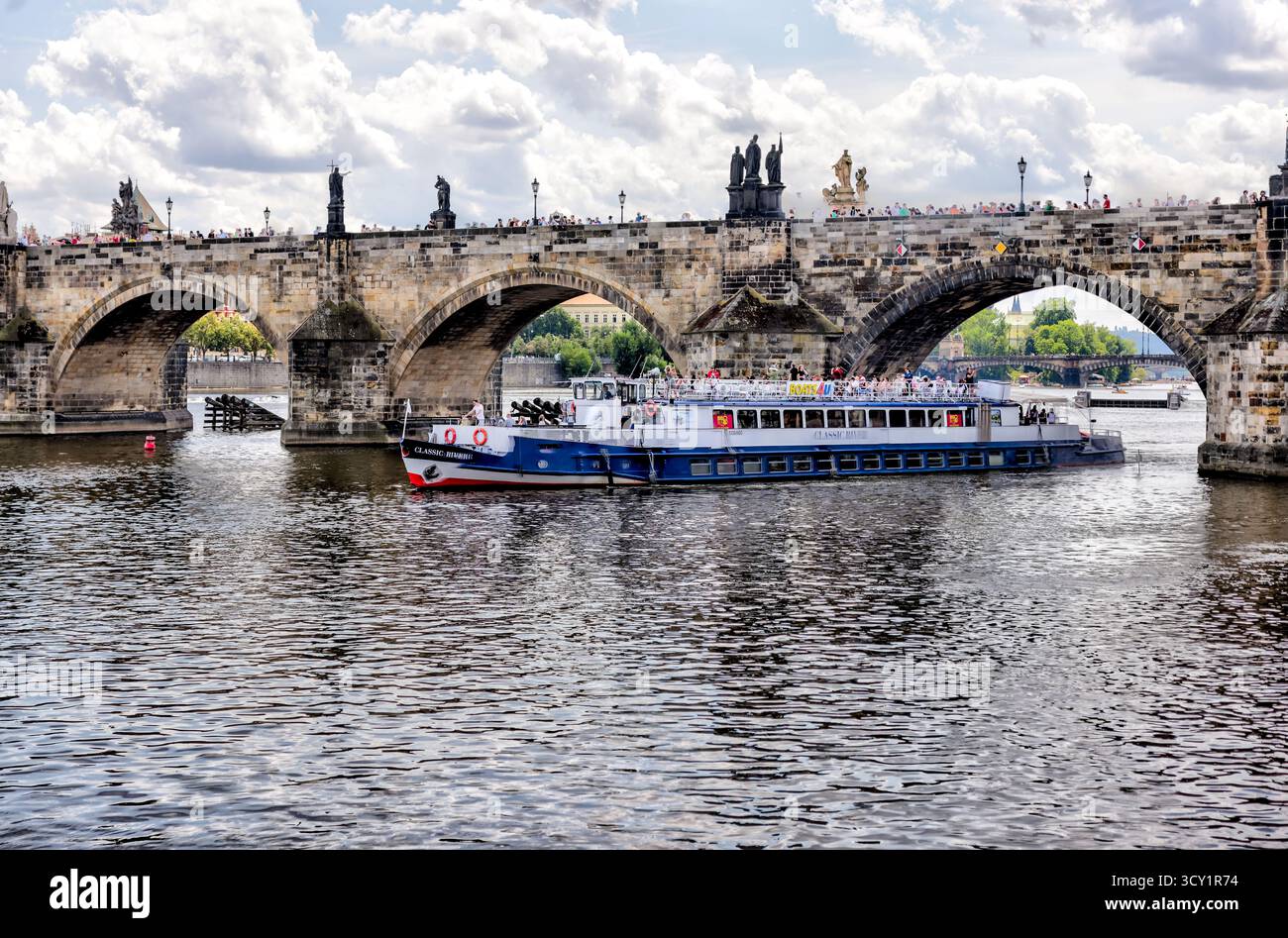 Bootstour unter der Karlsbrücke auf der Moldau in Prag, Tschechien, mit Menschenmassen, die an einem Sommertag auf der historischen Brücke spazieren gehen. Stockfoto