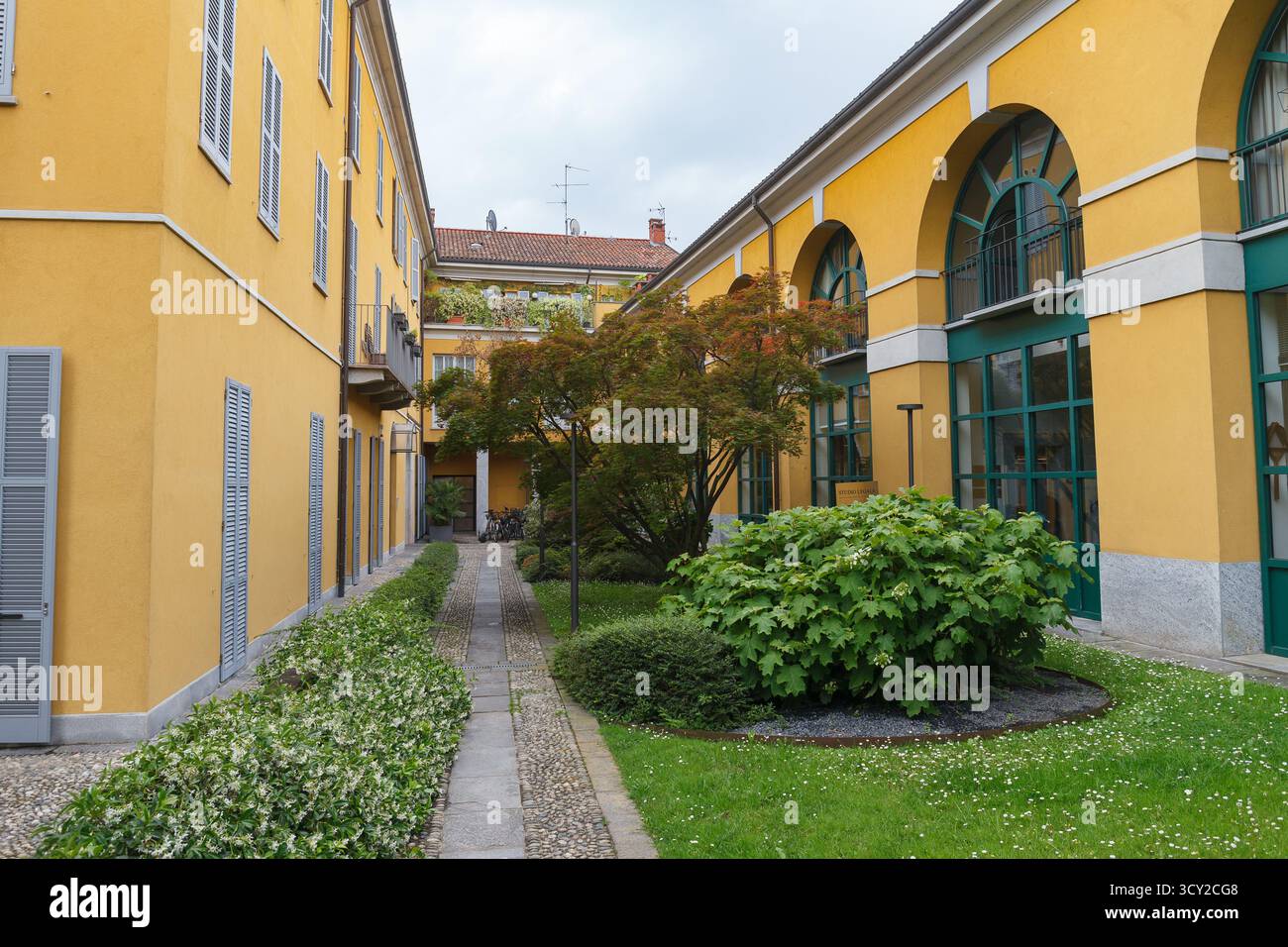 Grünanlage im Innenhof mit Wegen, historischen Steinbauten, gelber Farbe, Jahr XX Jahrhundert. Monza, Italien. Stockfoto
