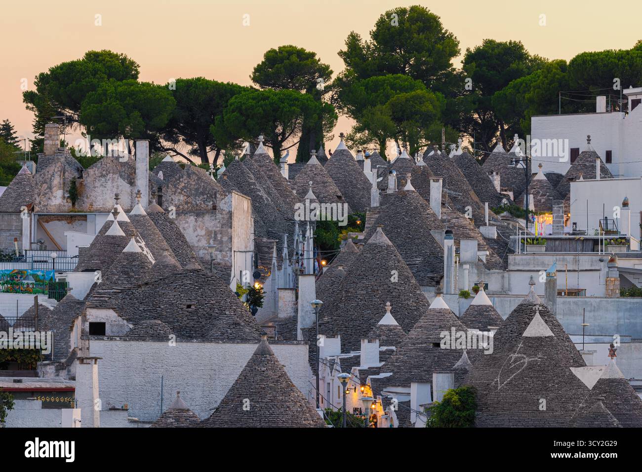 Eine wunderschöne Abendszene in Alberobello, Apulien, Italien, mit den traditionellen Trulli-Häusern, die sanft in warmem Licht leuchten. Die konischen Dächer und weiß Stockfoto Eine wunderschöne Abendszene in Alberobello, Apulien, Italien, mit den traditionellen Trulli-Häusern, die sanft in warmem Licht leuchten. Die konischen Dächer und weiß Stockfoto