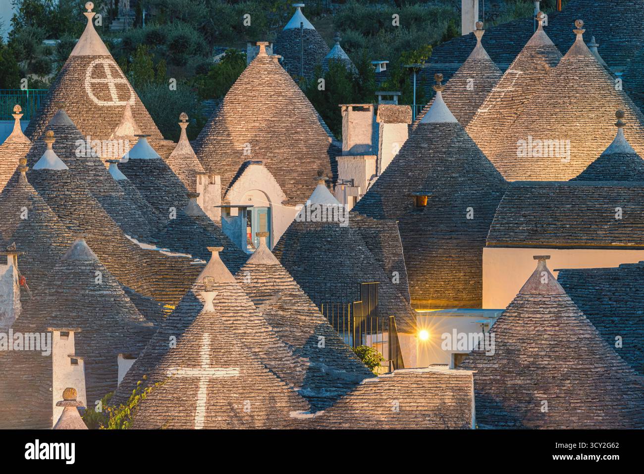 Eine wunderschöne Abendszene in Alberobello, Apulien, Italien, mit den traditionellen Trulli-Häusern, die sanft in warmem Licht leuchten. Die konischen Dächer und weiß Stockfoto Eine wunderschöne Abendszene in Alberobello, Apulien, Italien, mit den traditionellen Trulli-Häusern, die sanft in warmem Licht leuchten. Die konischen Dächer und weiß Stockfoto