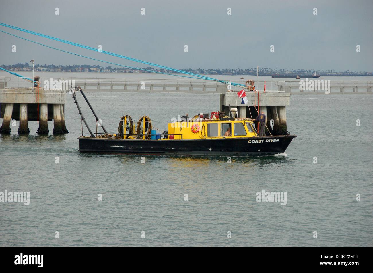 Ein gelb-schwarzes Coast Diver Boot in der Nähe eines Piers in ruhigen Küstengewässern, ausgestattet mit Tauchausrüstung und Fahnen, die für Unterwasseraktivitäten verwendet werden Stockfoto