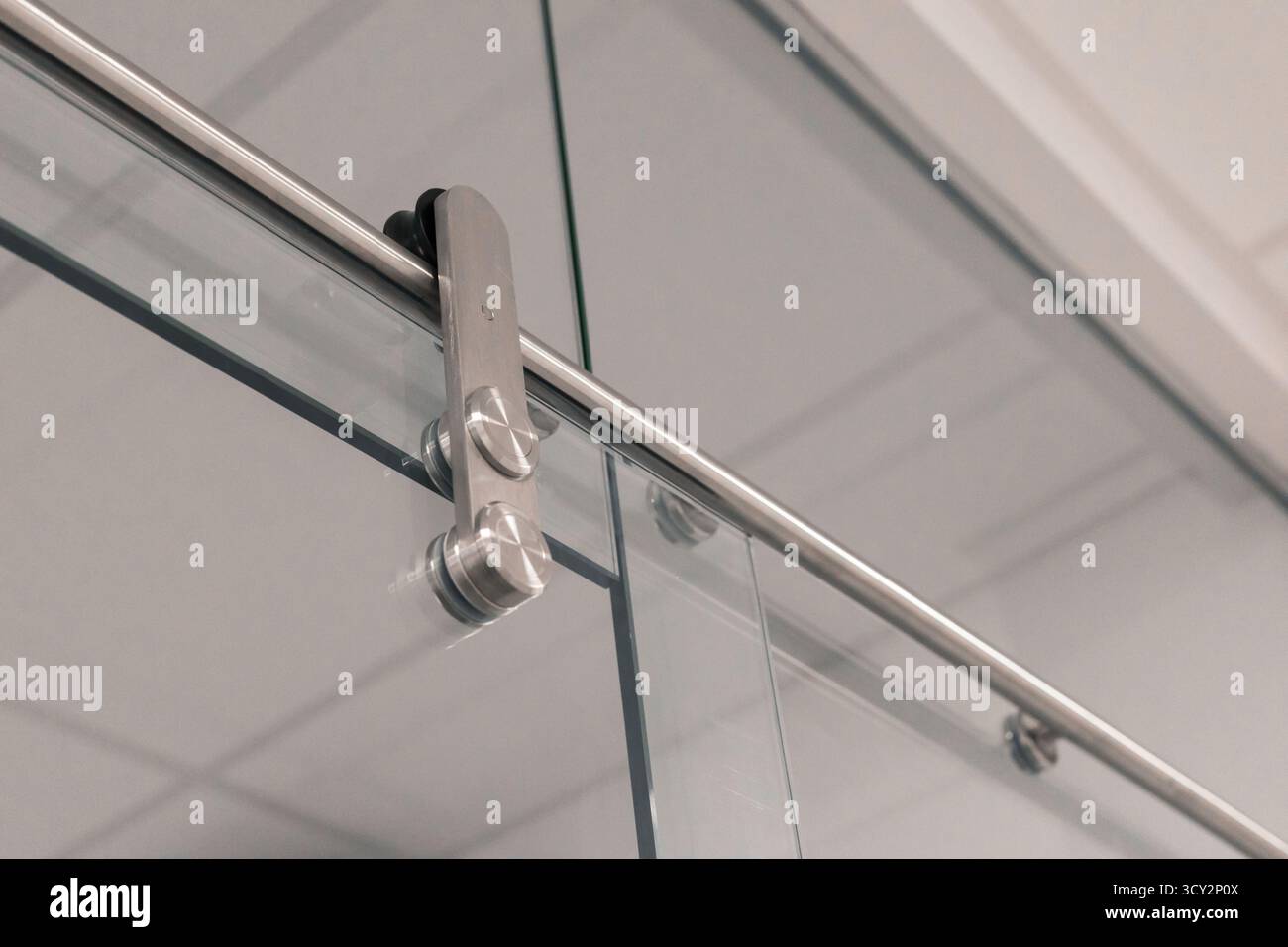 Die Beschläge der Schiebetüren aus Glas mit polierten Metallkomponenten und einer durchsichtigen Glasscheibe vor einem hellen Innenhintergrund aus nächster Nähe. Dies Stockfoto