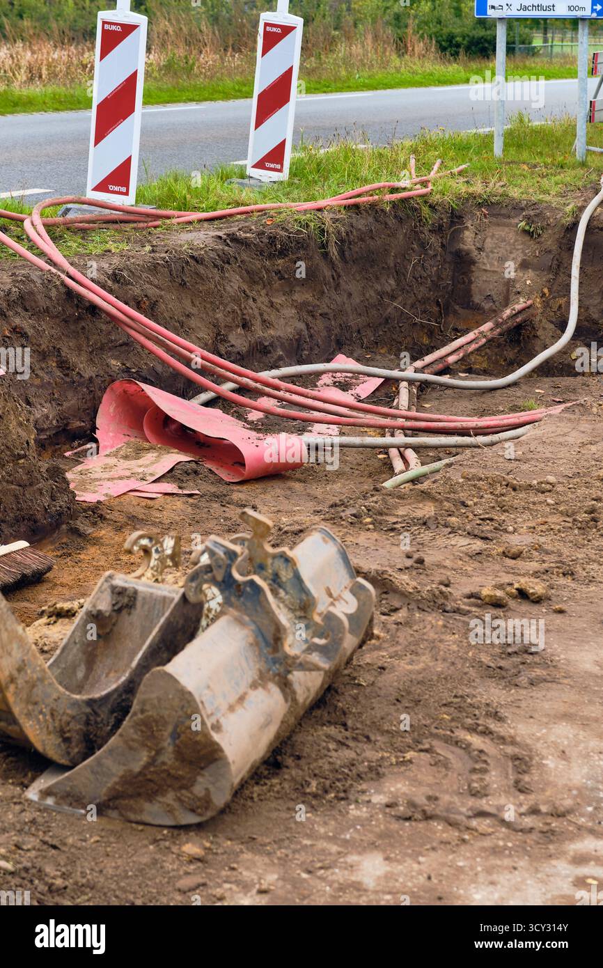 Roden, Niederlande; 8. Oktober 2025: Aushubgraben für neues 10-kV-Stromnetz mit sichtbaren roten Aluminium-Dreiphasenkabeln Minibagger b Stockfoto