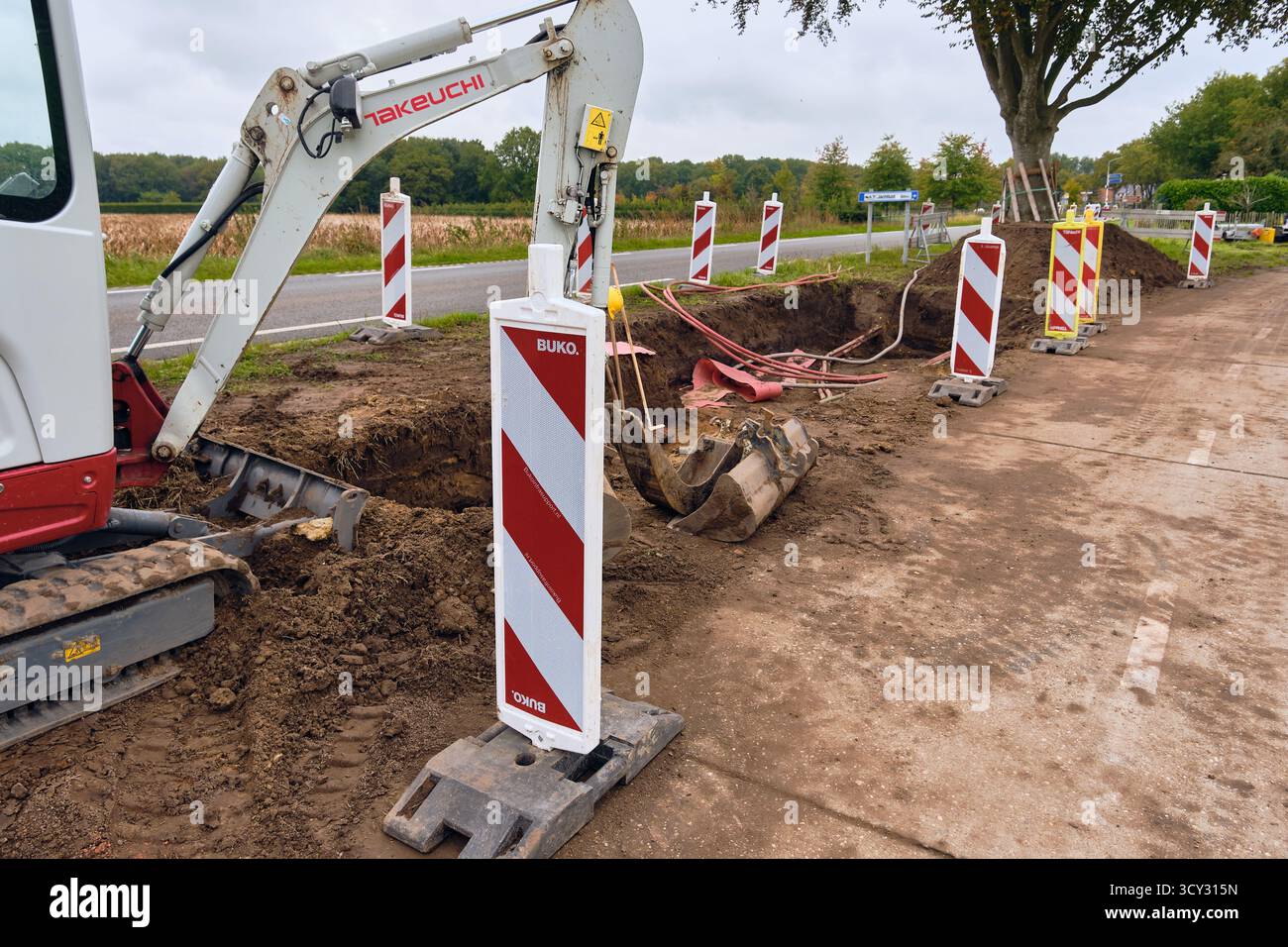 Roden, Niederlande; 8. Oktober 2025: Aushubgraben für neues 10-kV-Stromnetz mit sichtbaren roten Aluminium-Dreiphasenkabeln und Takeuchi min Stockfoto